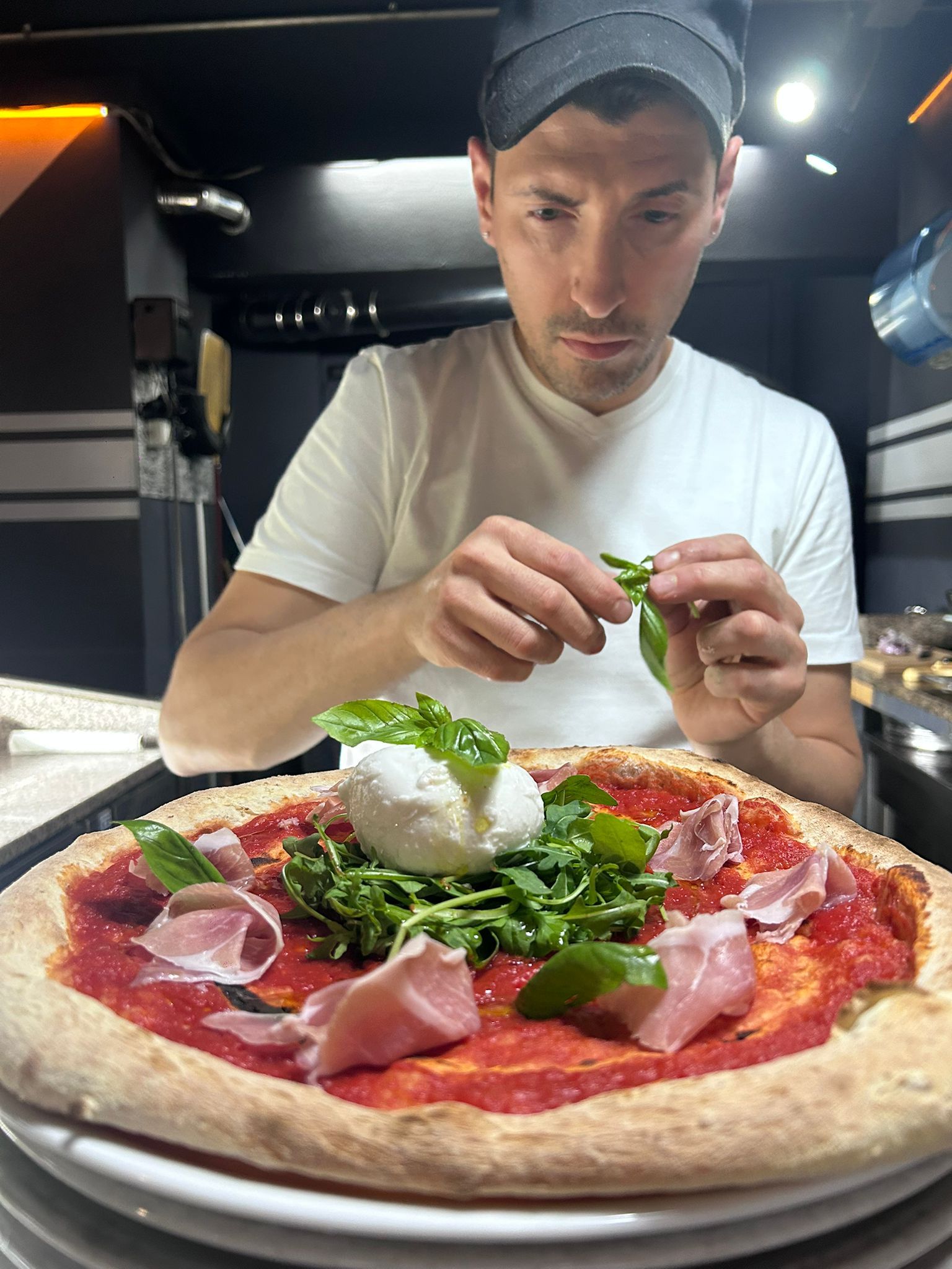Uno chef guarnisce la pizza con basilico e burrata nella cucina di un ristorante.