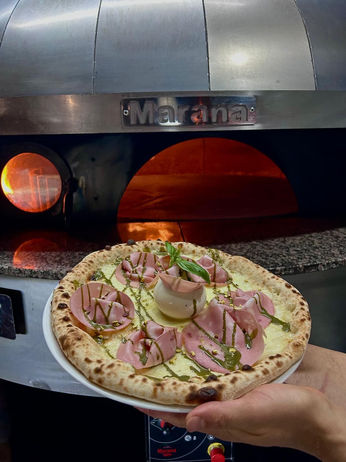 Pizza con prosciutto e basilico cotta davanti al forno a legna.