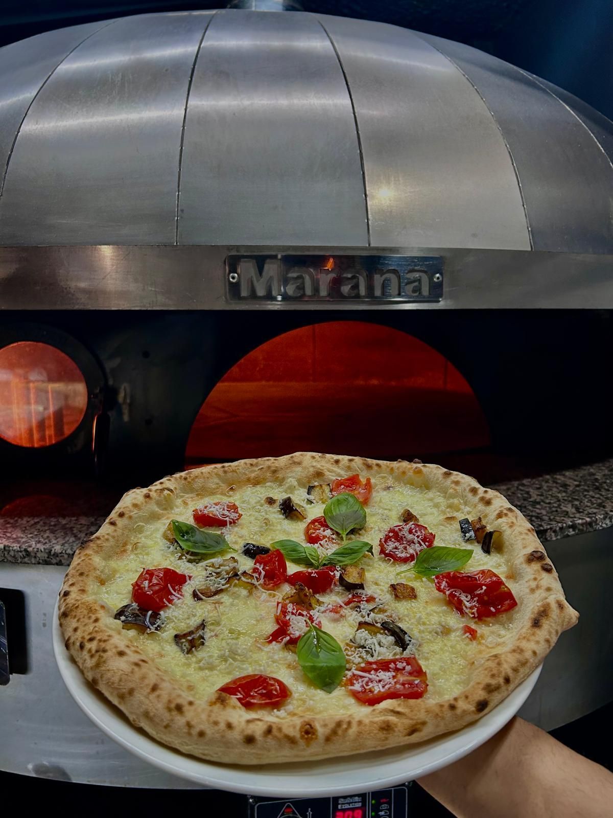 Pizza cotta nel forno a legna. La pizza è condita con pomodoro, basilico e formaggio.
