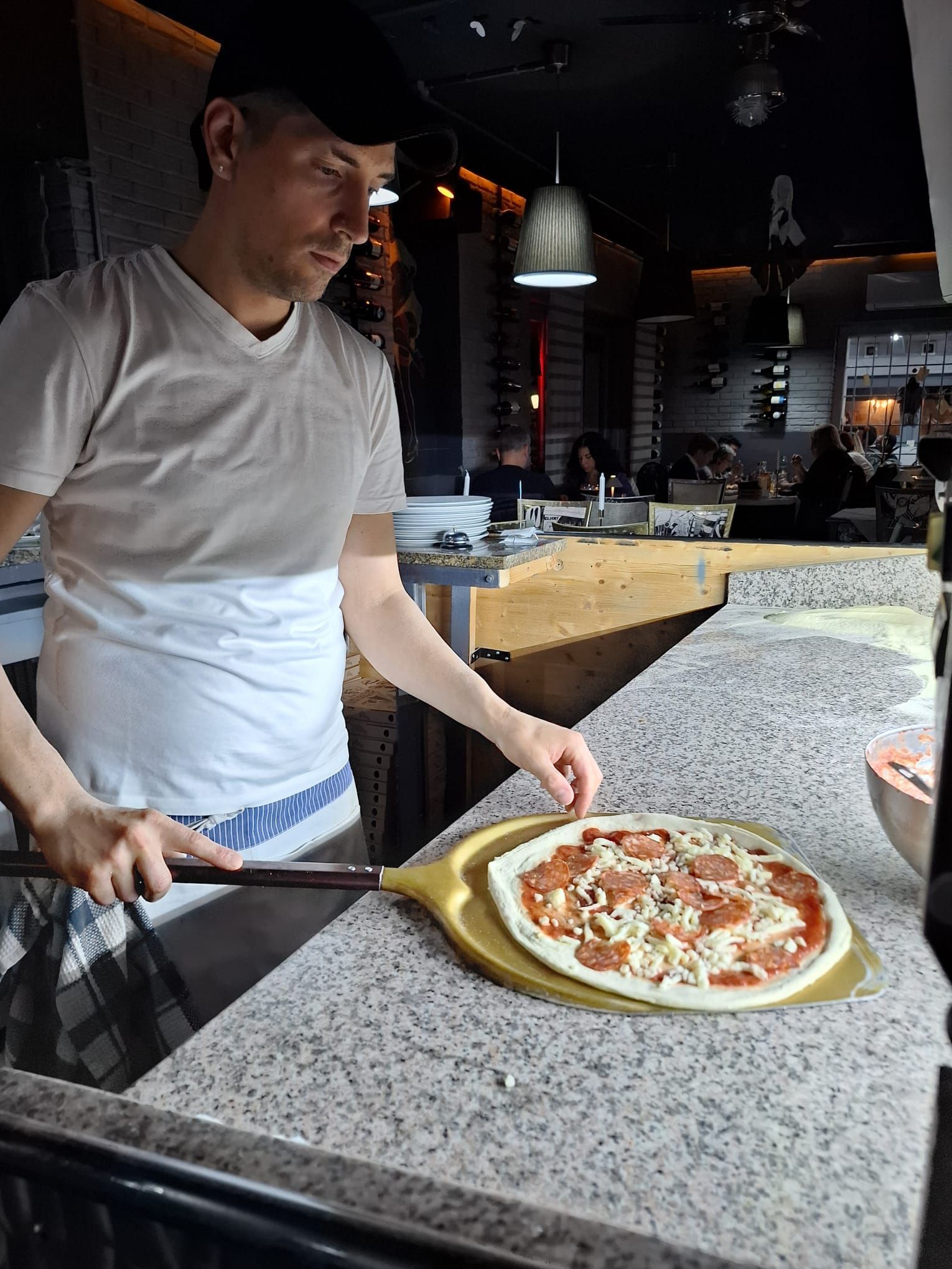 Uno chef prepara la pizza e la posiziona su una pala, all'interno della cucina di un ristorante.