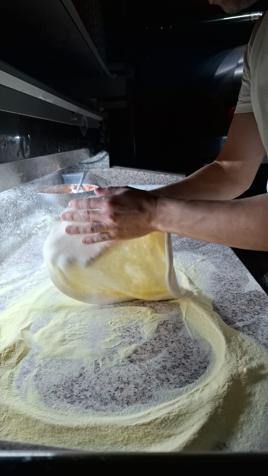 Una persona stende l'impasto della pizza su una superficie infarinata.