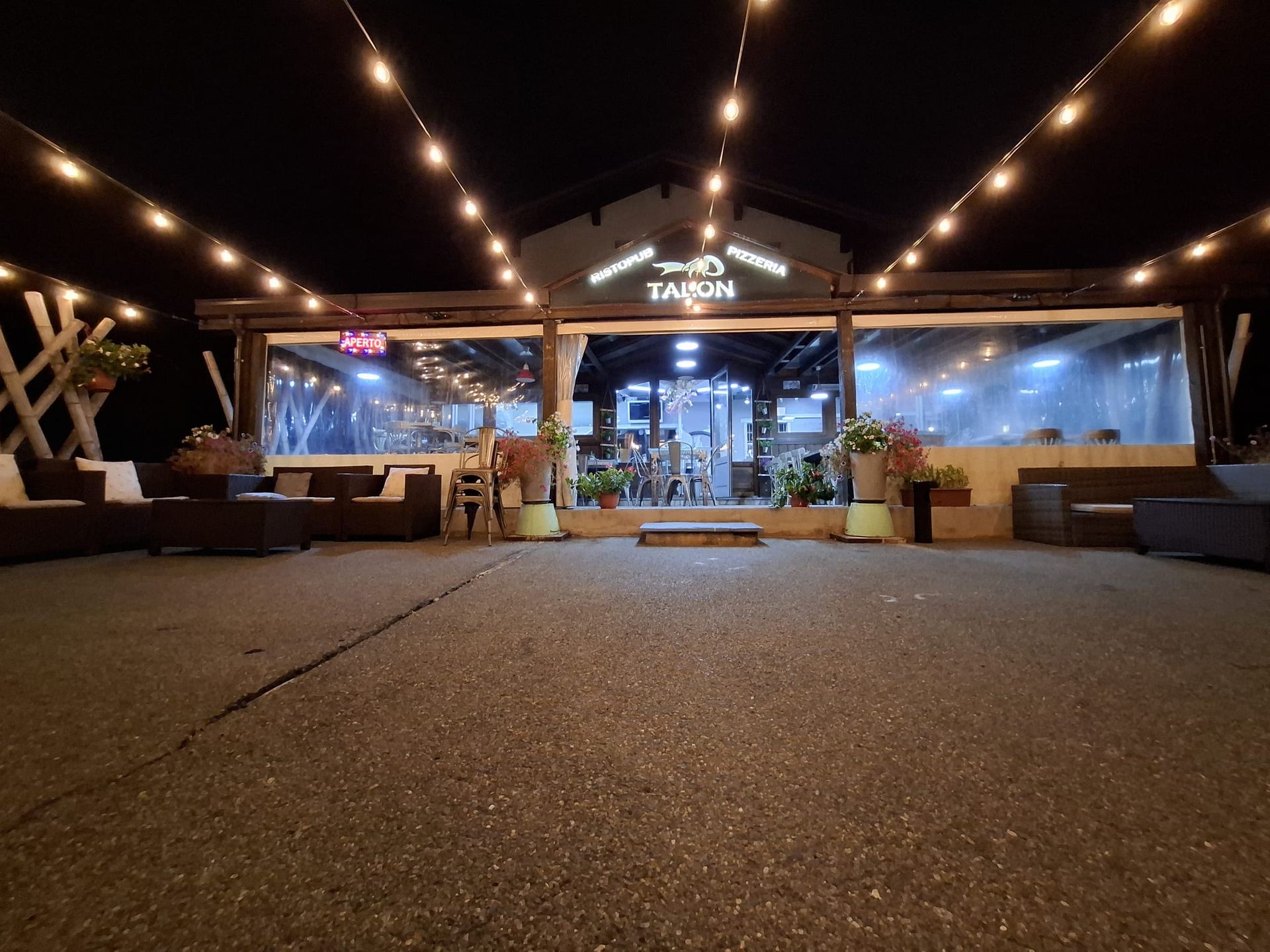 Ristorante all'aperto di notte, luci a ghirlanda, area salotto, finestra trasparente, insegna 