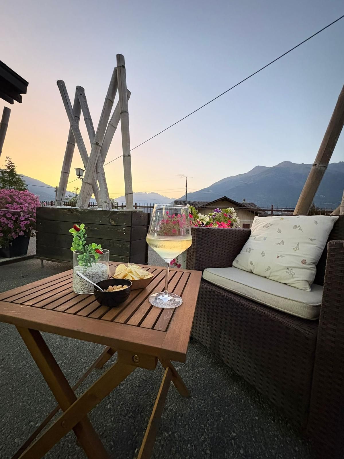 Un tavolo con spuntini e vino bianco su un patio con vista sulle montagne al tramonto.