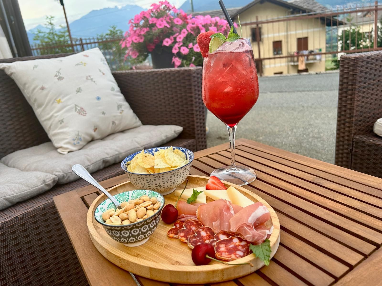 Tagliere di cocktail e salumi su un tavolo di legno, con vista sulle montagne.