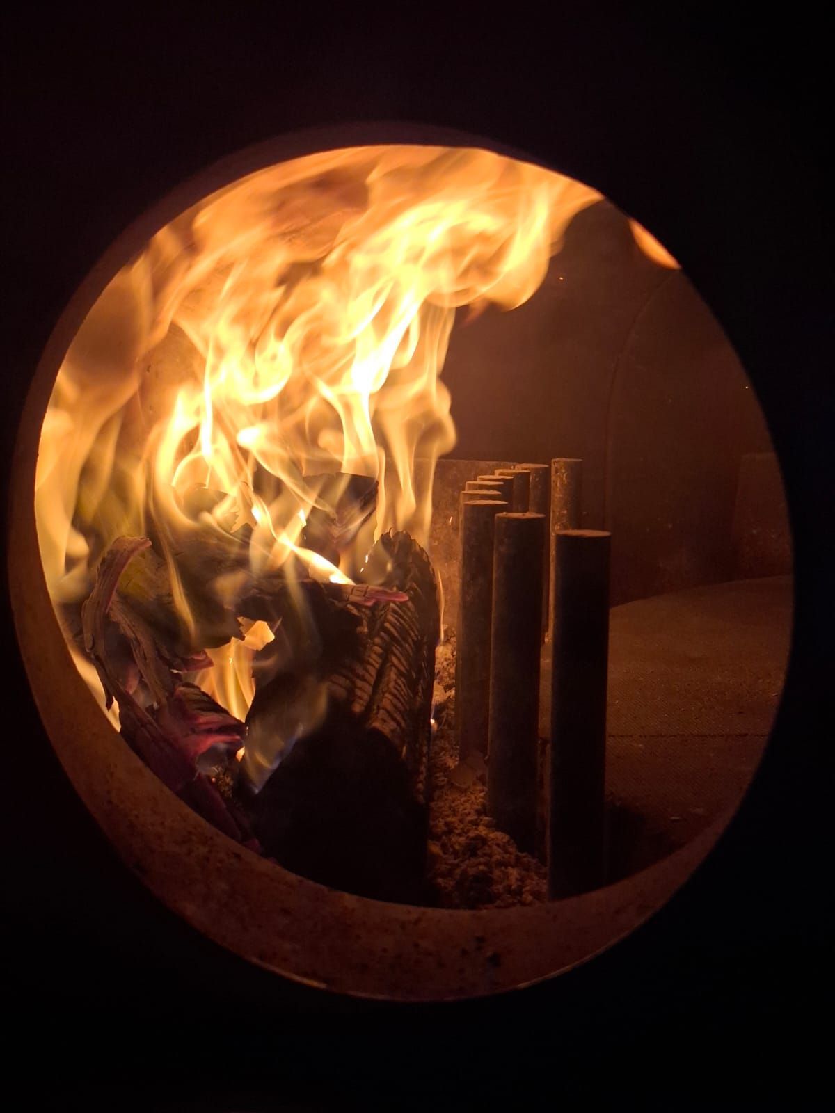 Fuoco che arde in un recinto metallico circolare con fiamme e fumo visibili.