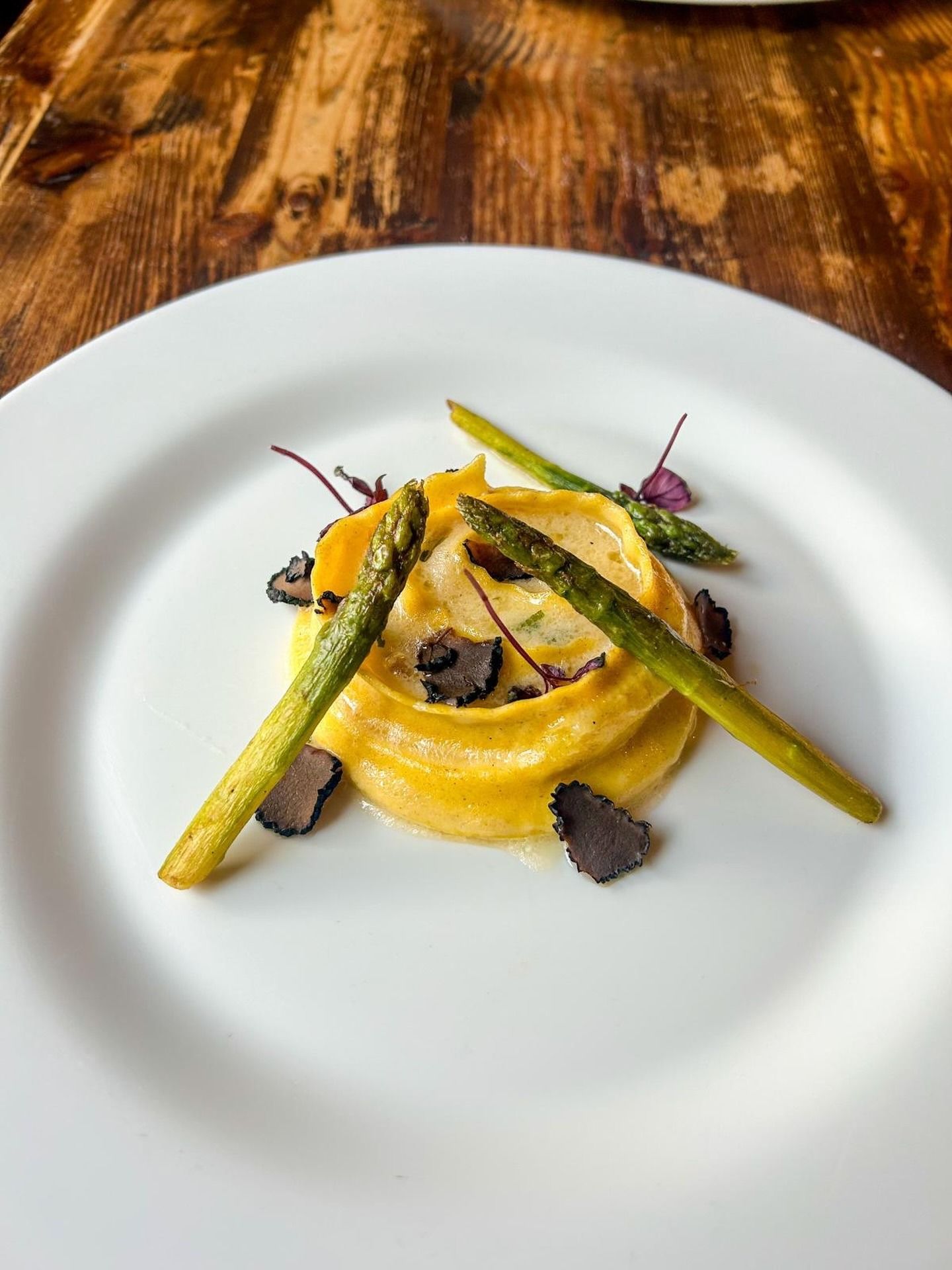 Piatto di pasta gialla con asparagi e scaglie di tartufo nero su piatto bianco, sfondo in legno.