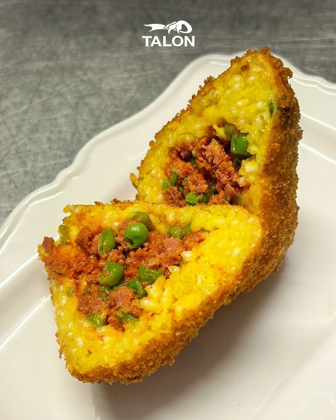 Arancino tagliato a metà, con ripieno di carne e piselli; esterno fritto e dorato.