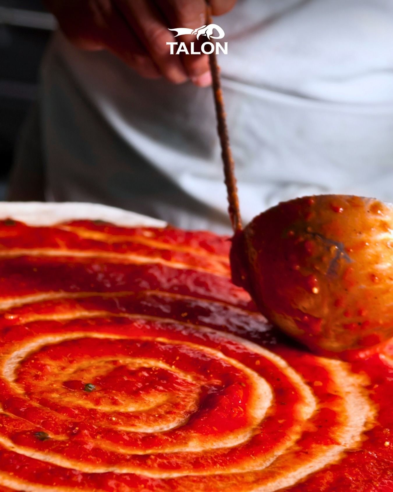 Persona che spalma la salsa di pomodoro sull'impasto con un cucchiaio.