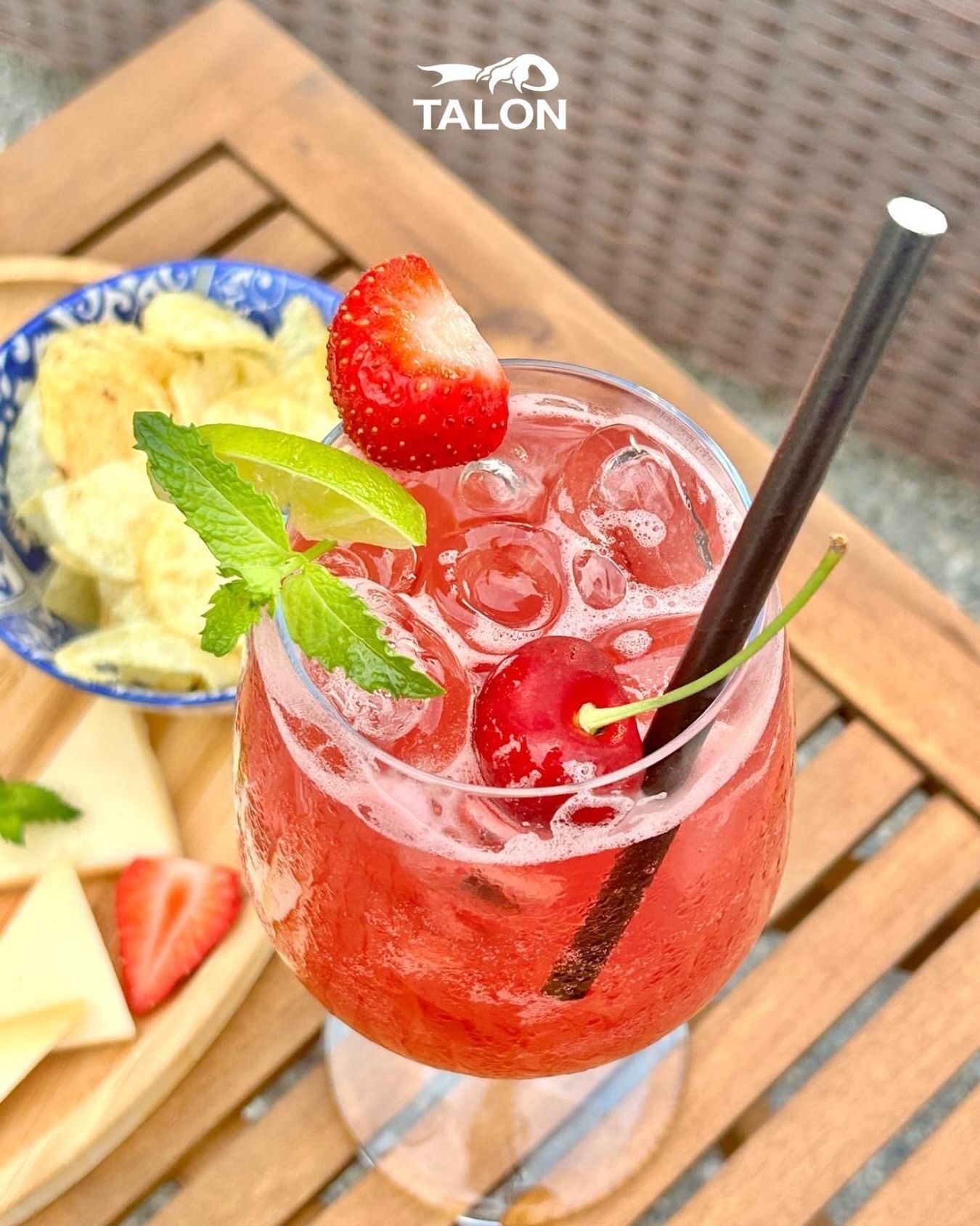 Cocktail rosso con fragola, ciliegia, lime, menta e cannuccia, servito con degli stuzzichini.
