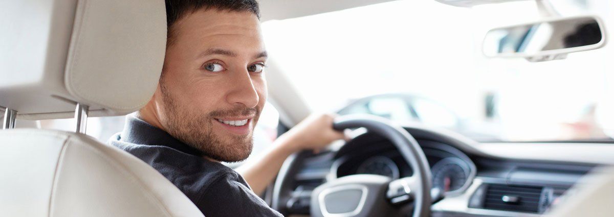 A man is sitting in the driver 's seat of a car and smiling.