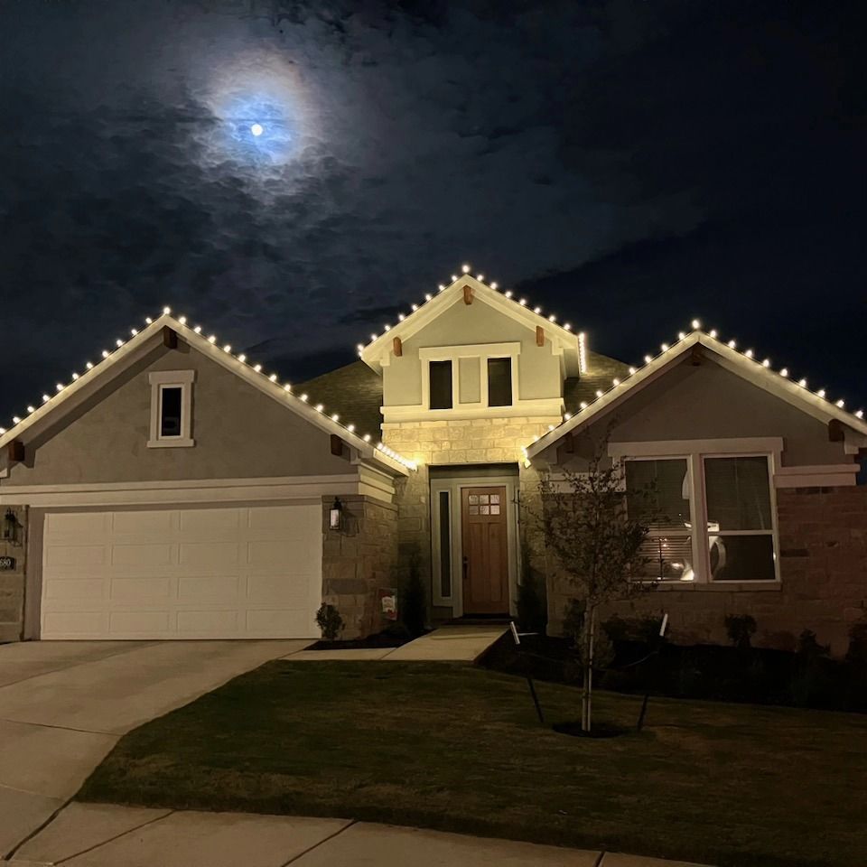 House with white Christmas lights on roof, lit by a full moon in night sky.