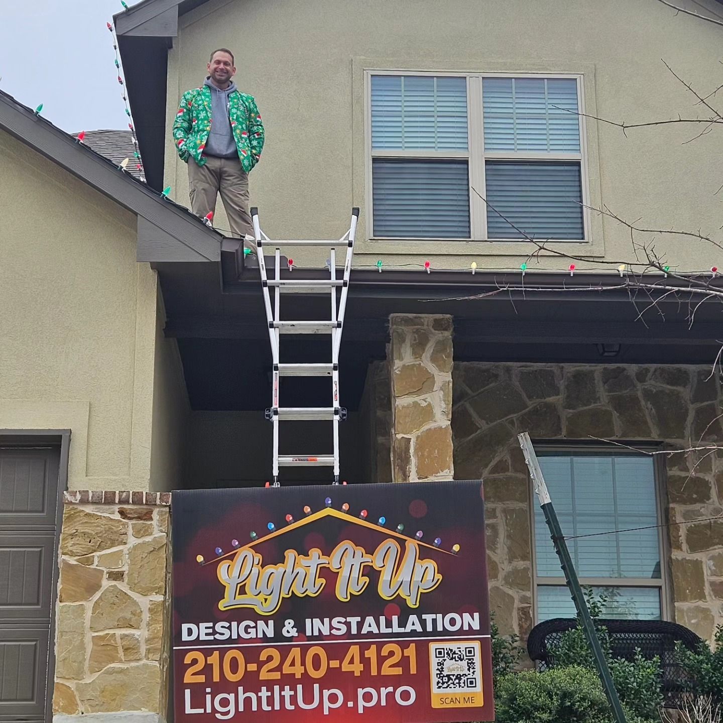 Man on a roof installing Christmas lights, with ladder and business sign for 