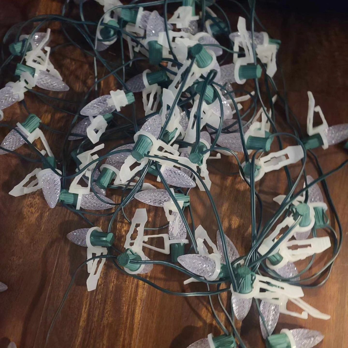 Tangled string of white and purple Christmas lights with green cords and white clips, on a wooden surface.