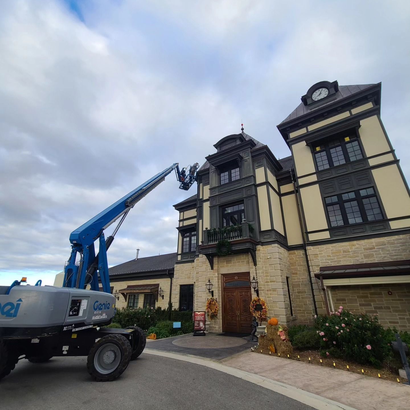 Blue lift reaching towards a multi-story building for maintenance; cloudy sky.
