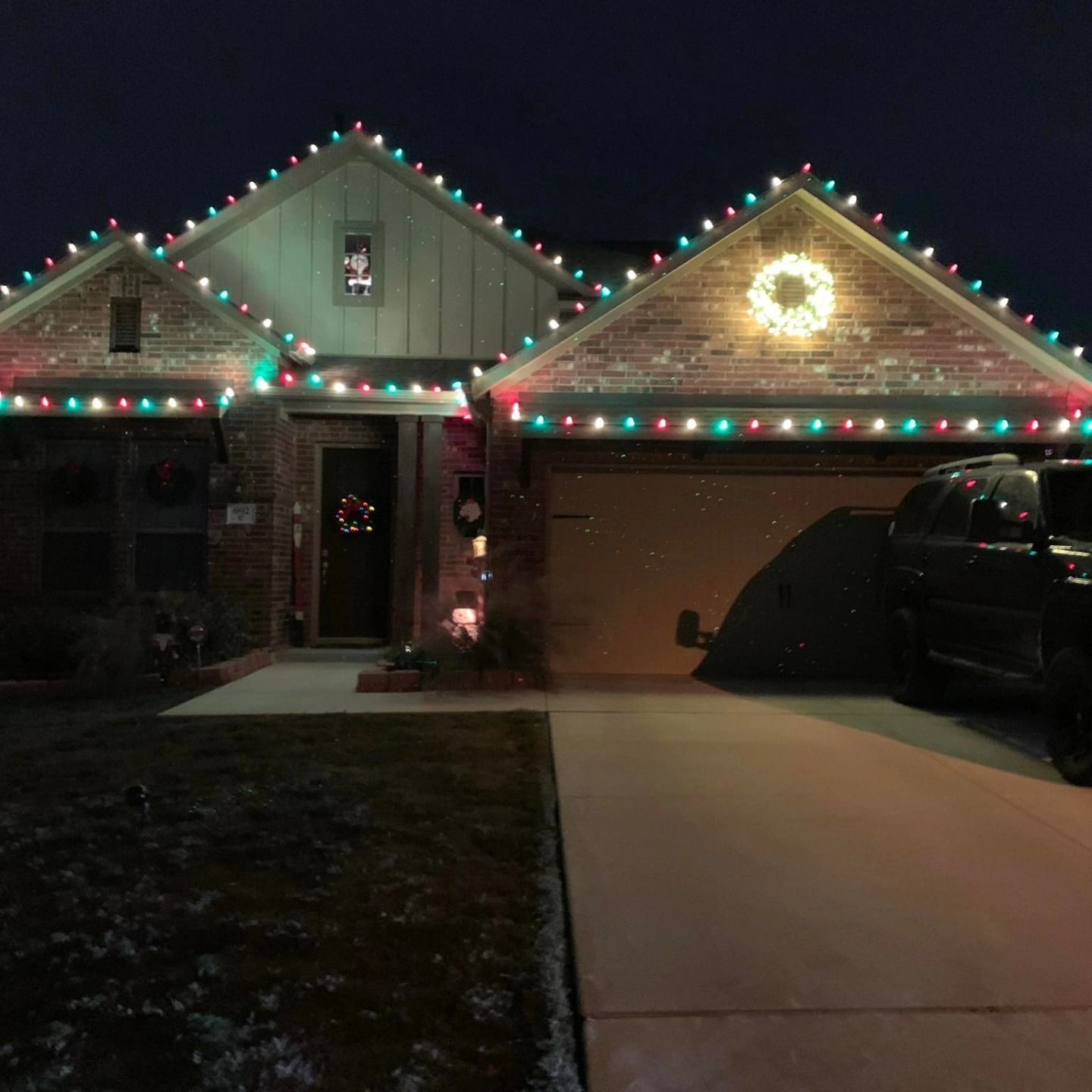 House decorated with red, green, and white Christmas lights along the roofline and a wreath on the door.