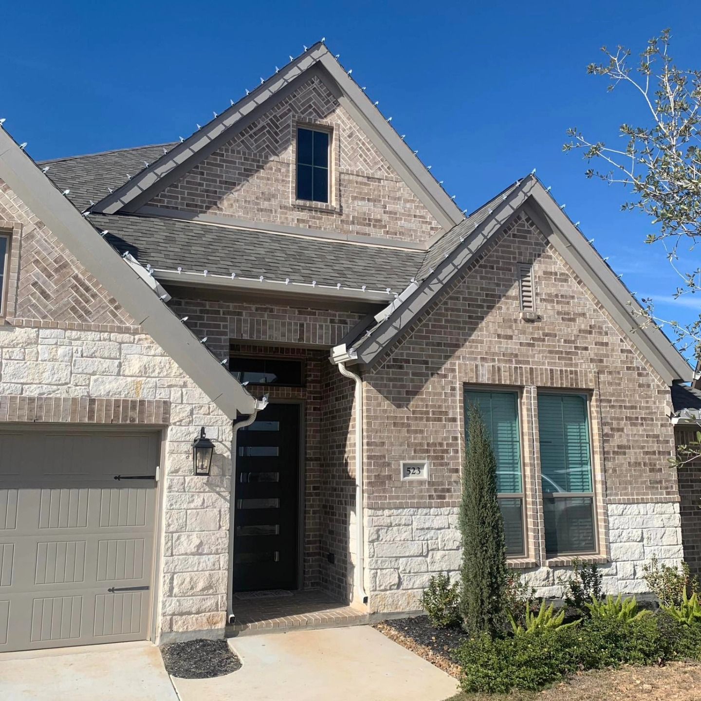 House exterior with brick and stone, blue sky, and small bushes.