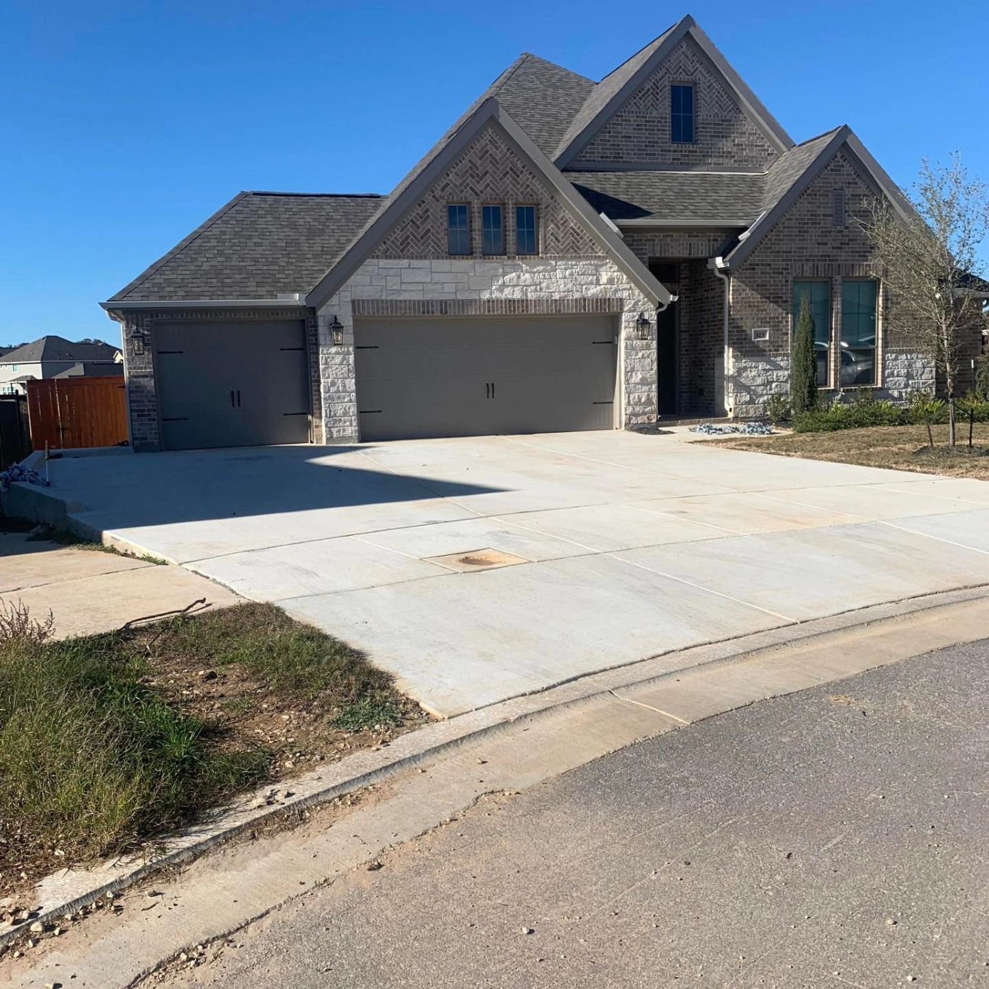 House with stone and brick facade, two-car garage, and concrete driveway on a sunny day.