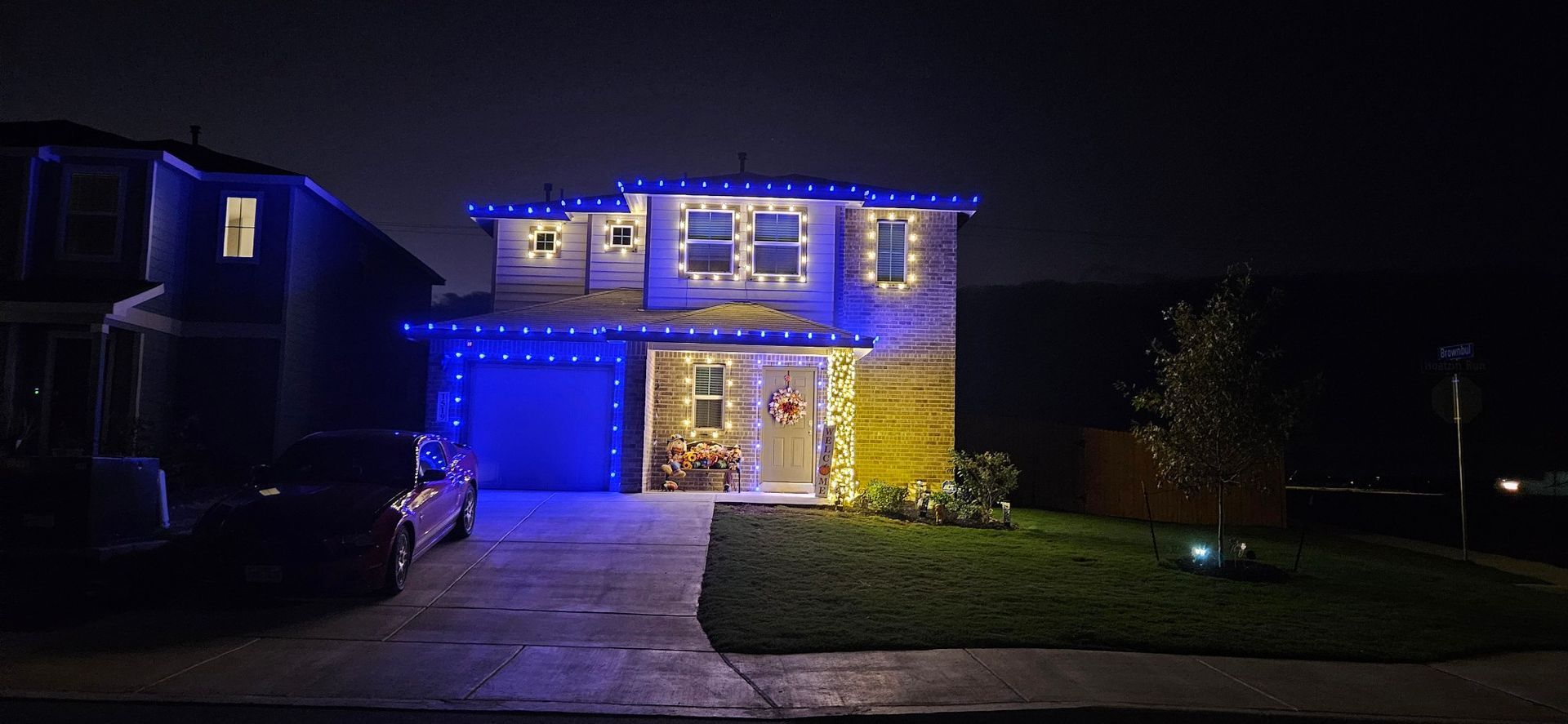 A house decorated with blue and white lights at night. Front yard with a car parked in the driveway.