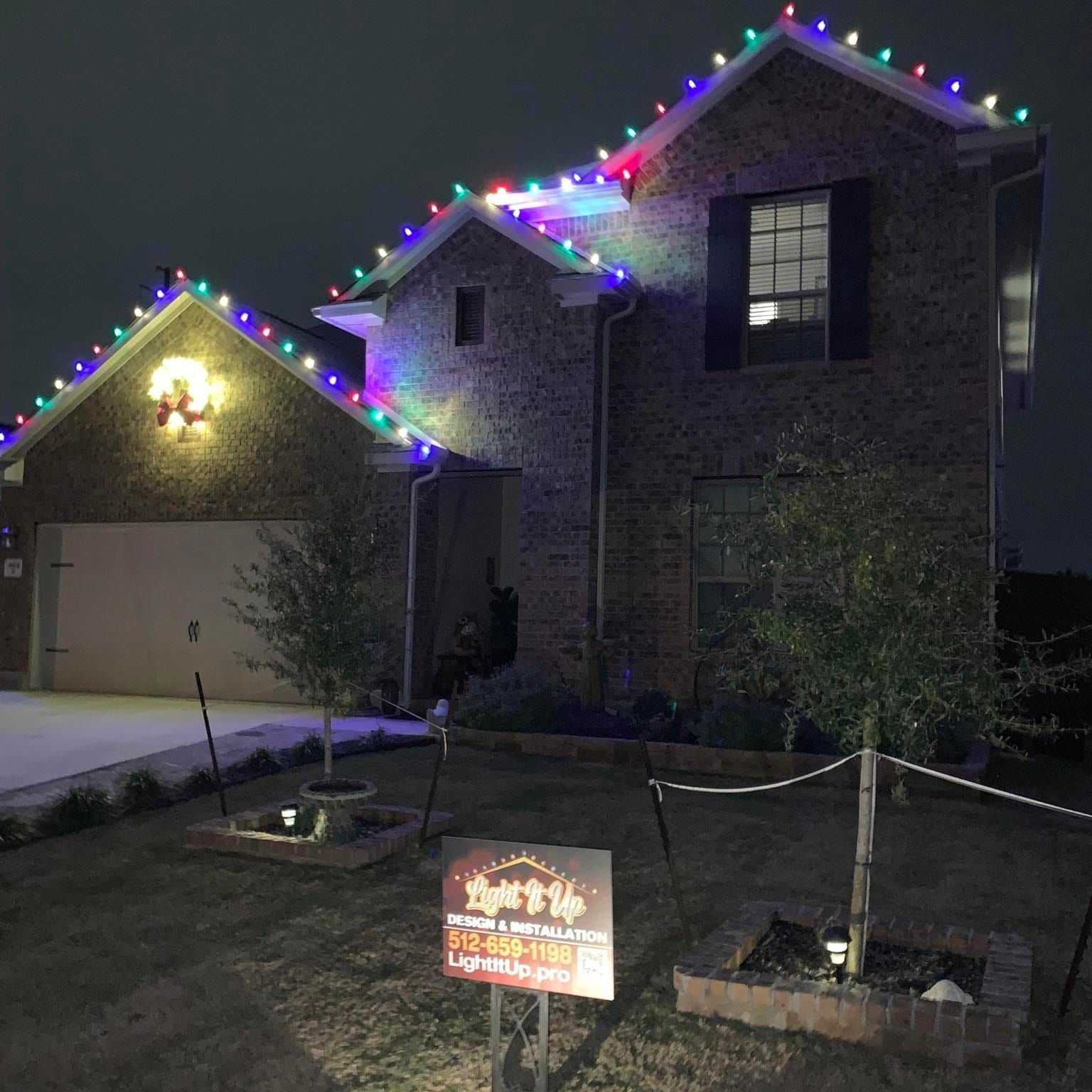 House decorated with colorful Christmas lights at night. Sign in the yard.