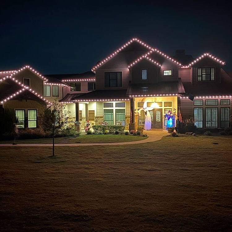 House at night with pink Christmas lights outlining roof and yard.