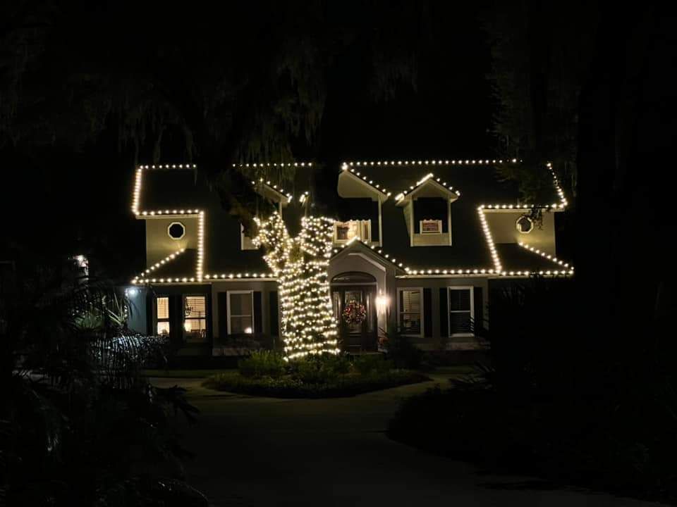 Two-story house illuminated by Christmas lights at night. Lit tree in front, lights along rooflines.