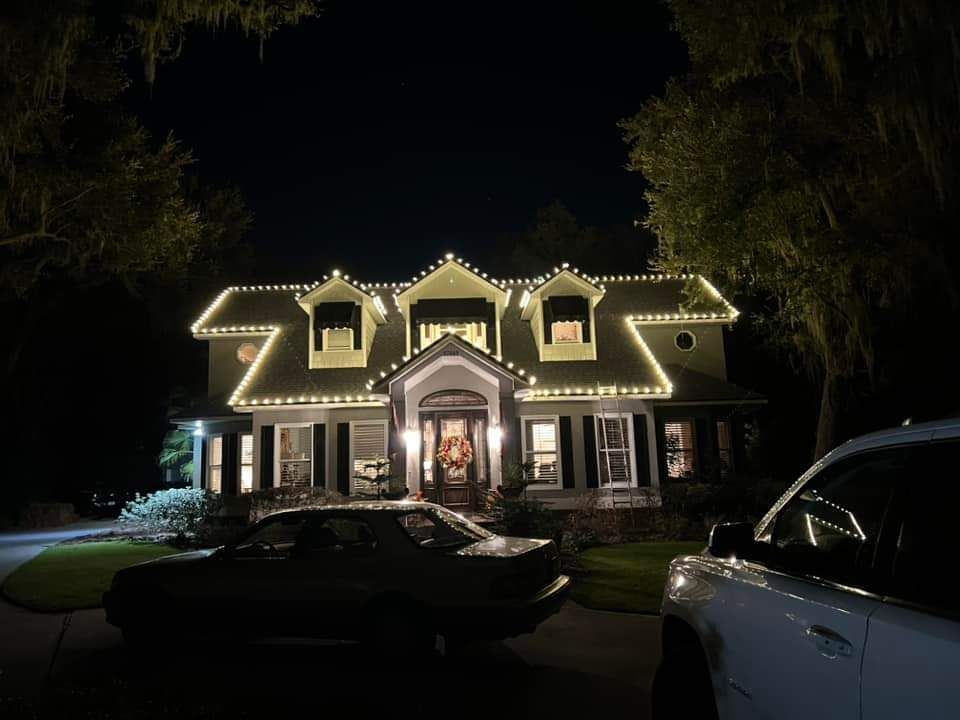 Night shot of a house decorated with white lights. A car sits in the driveway.