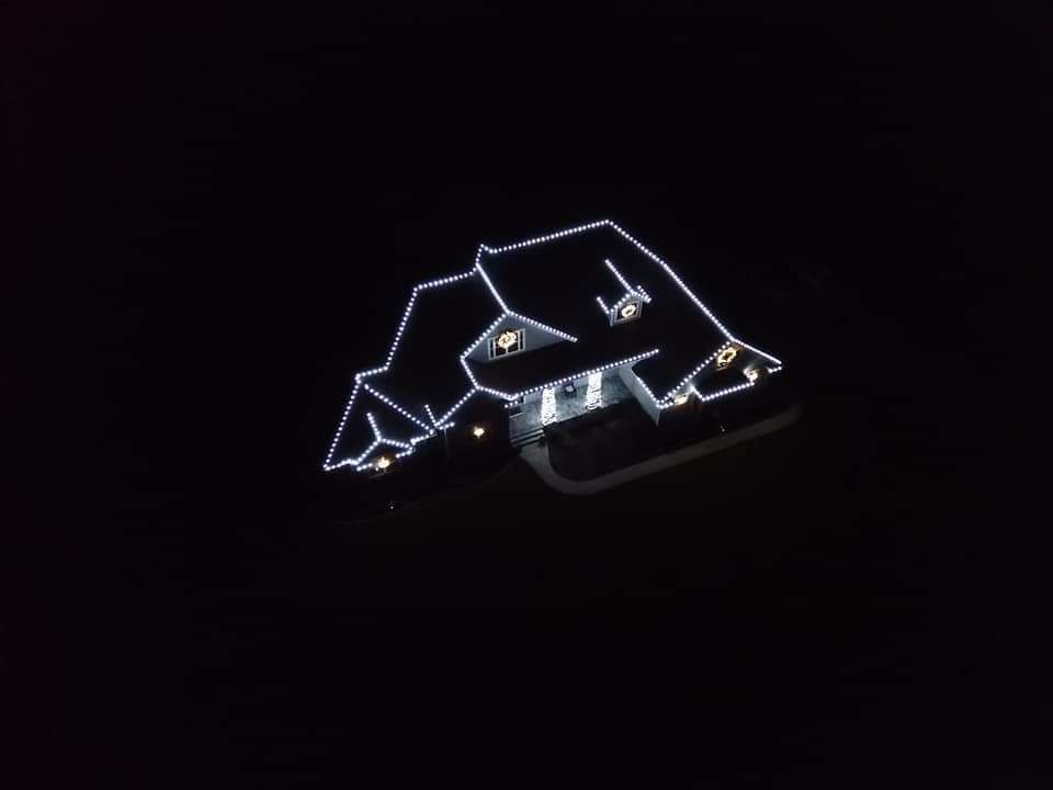 House outlined in white lights against a black night sky, lit for the holidays.