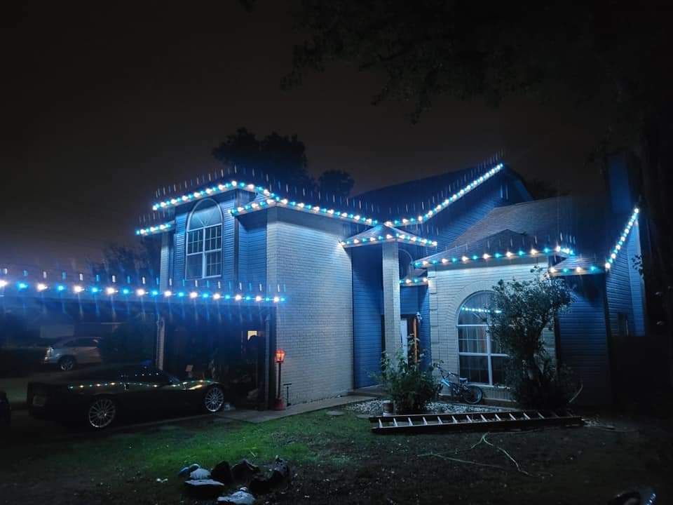 A blue house at night, decorated with blue Christmas lights, with a car parked in front.