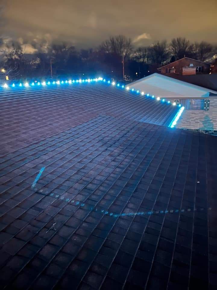Rooftop with rows of dark shingles. Blue lights outline the roof edges. Cloudy night sky.