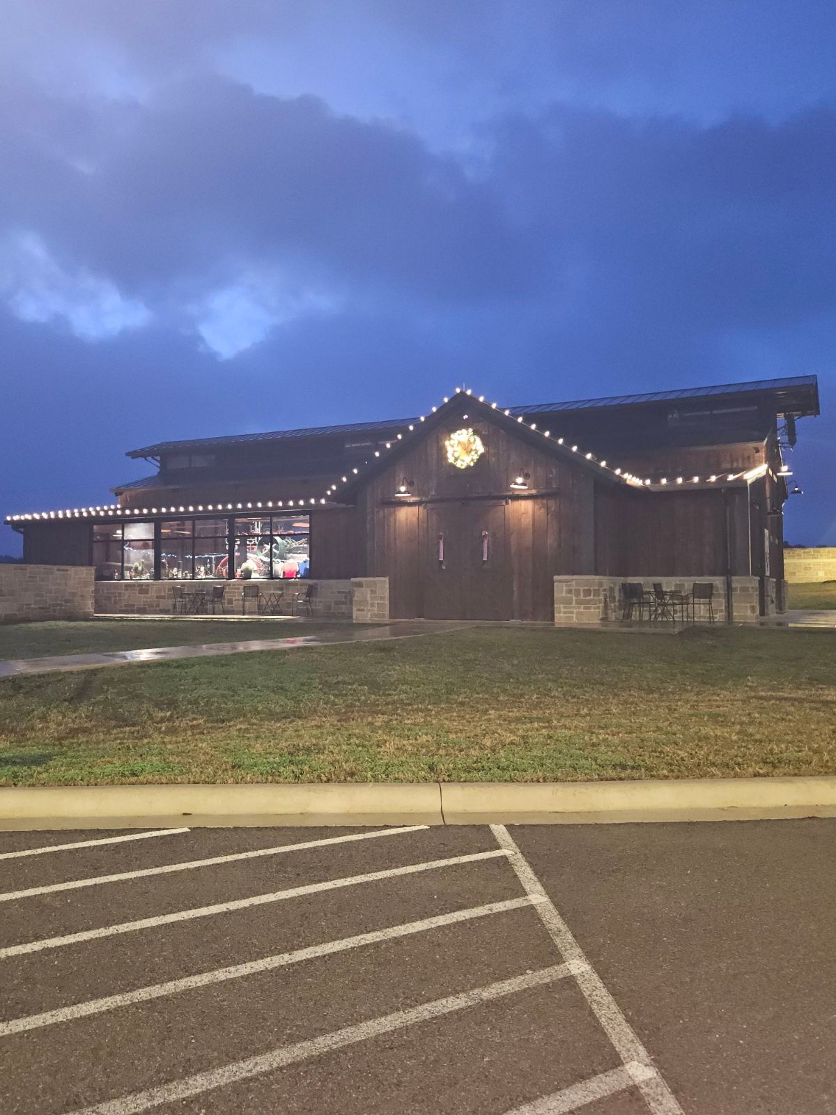 Dark wooden building with string lights, windows, and stone accents under a cloudy sky.