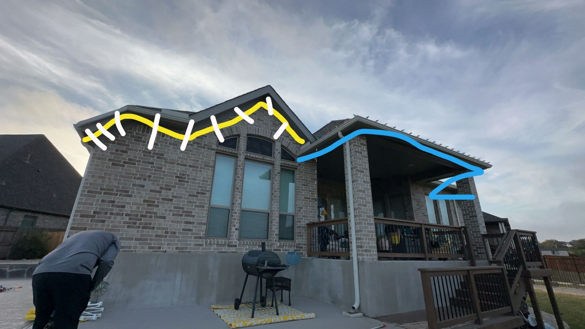 Person looking at a stone house with a porch and deck under a cloudy sky.