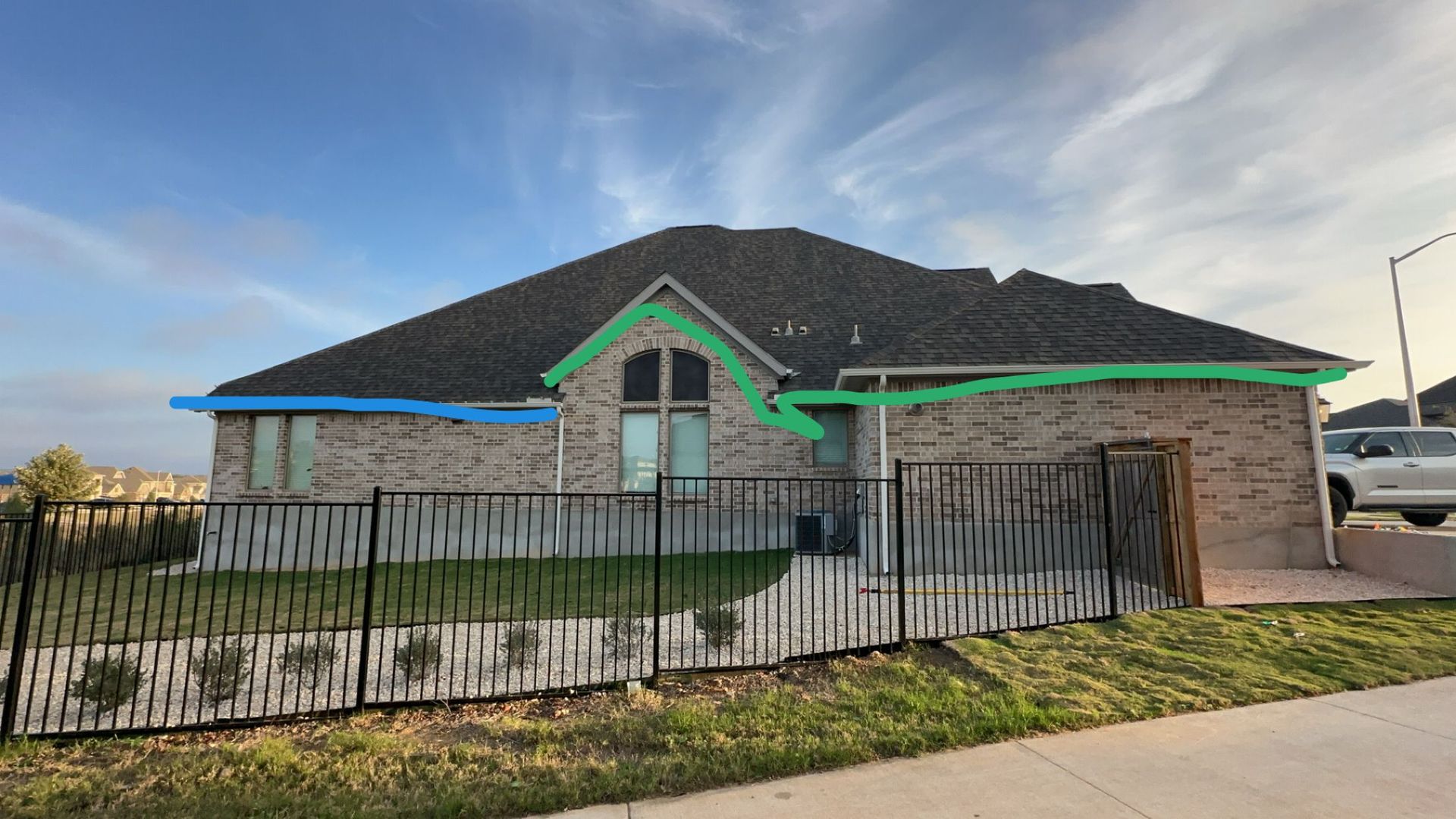 Brick house with a dark roof, blue and green trim, and a black fence.