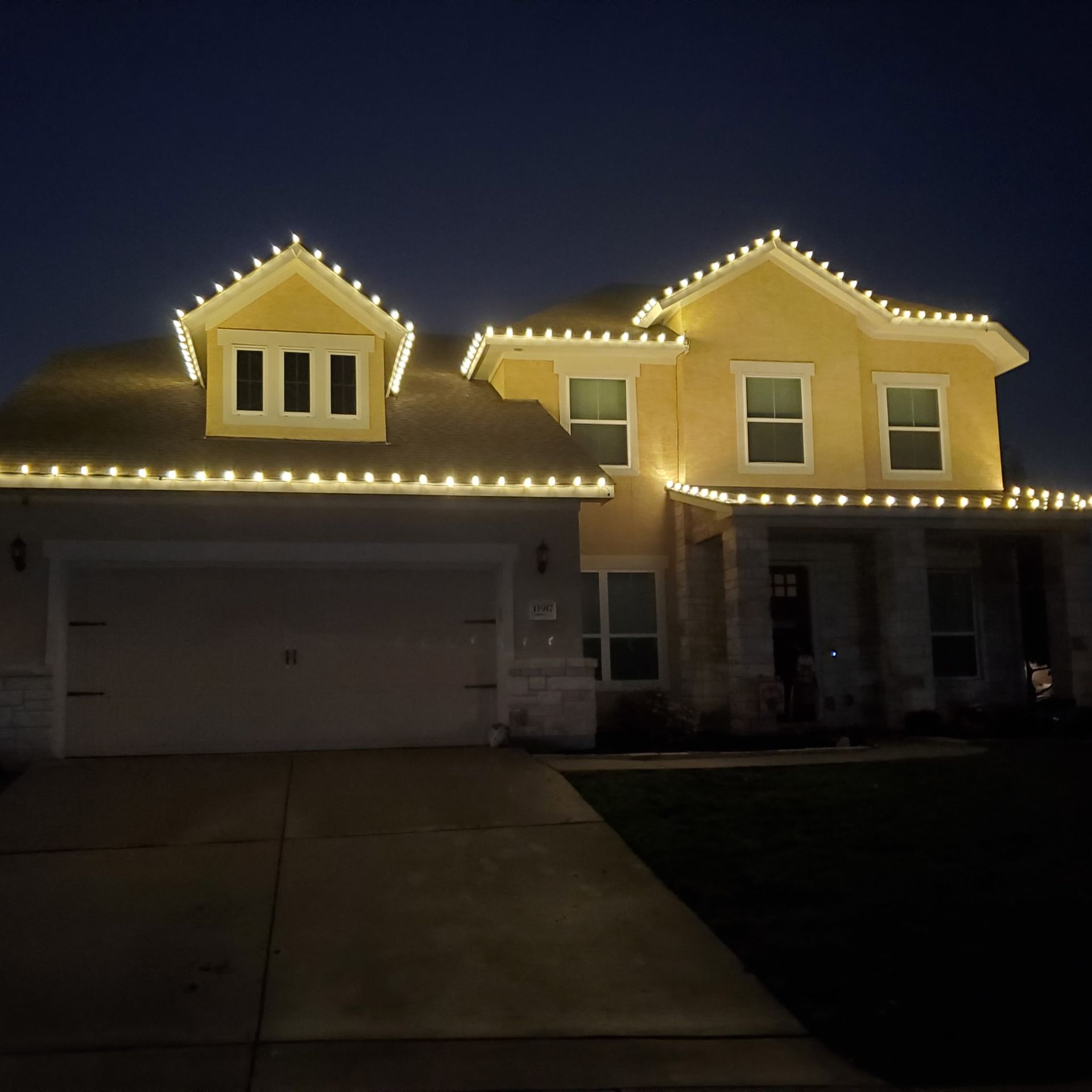 House at night with rooflines illuminated by warm white Christmas lights.