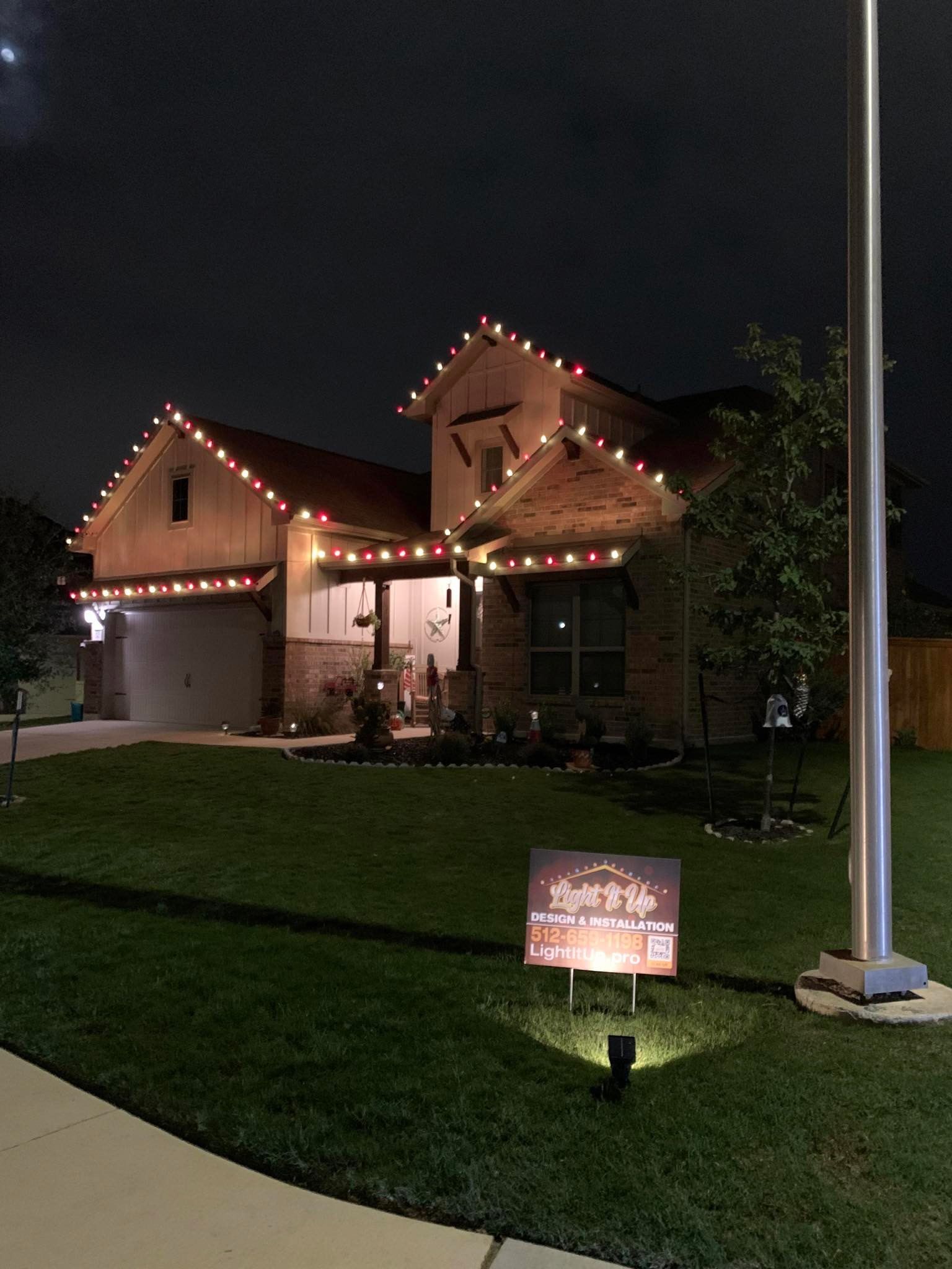 A house at night with Christmas lights, lawn sign, and a flagpole.