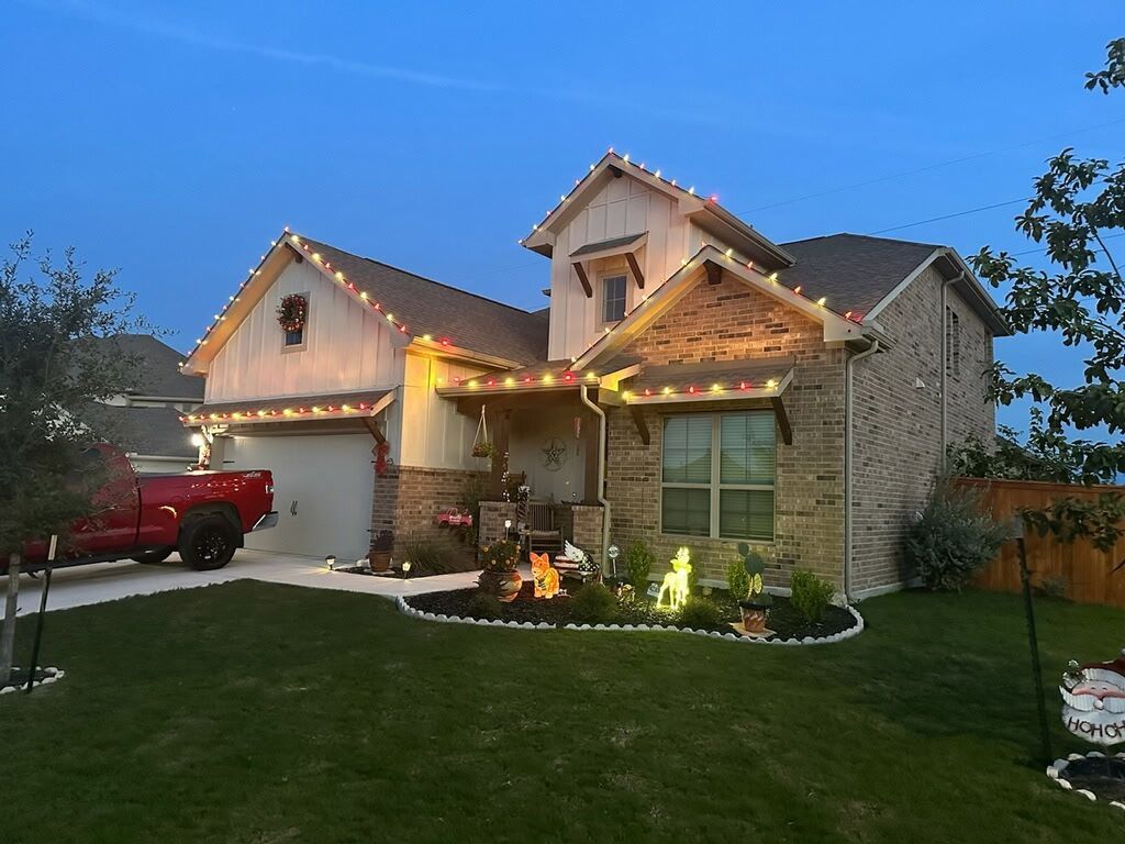 House decorated with Christmas lights; red truck in driveway, green lawn, and dusk sky.