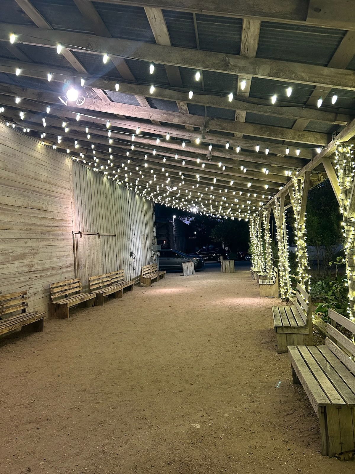 An outdoor walkway with string lights, benches, and a gravel path at night.