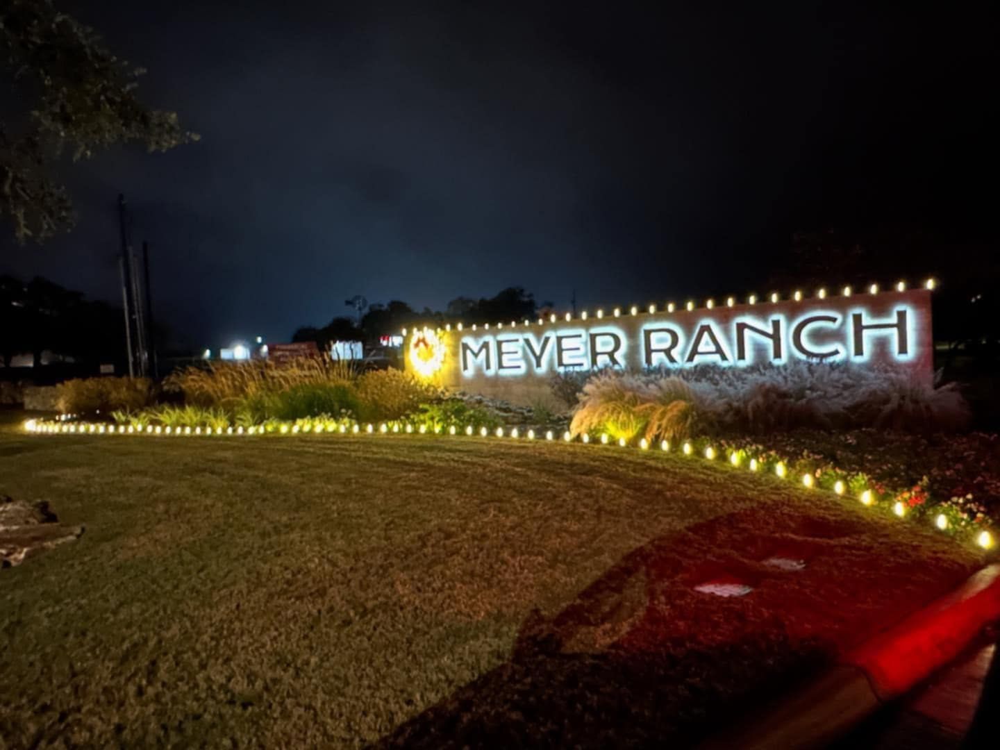 Meyer Ranch sign lit at night with illuminated letters and small lights outlining the landscaping.