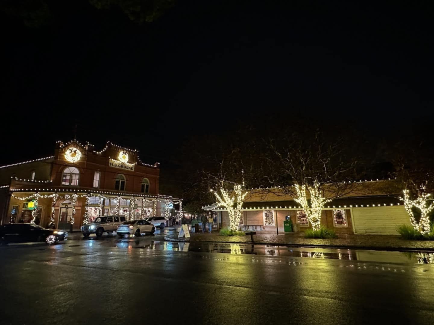 Night scene: Buildings decorated with lights reflecting on wet street.