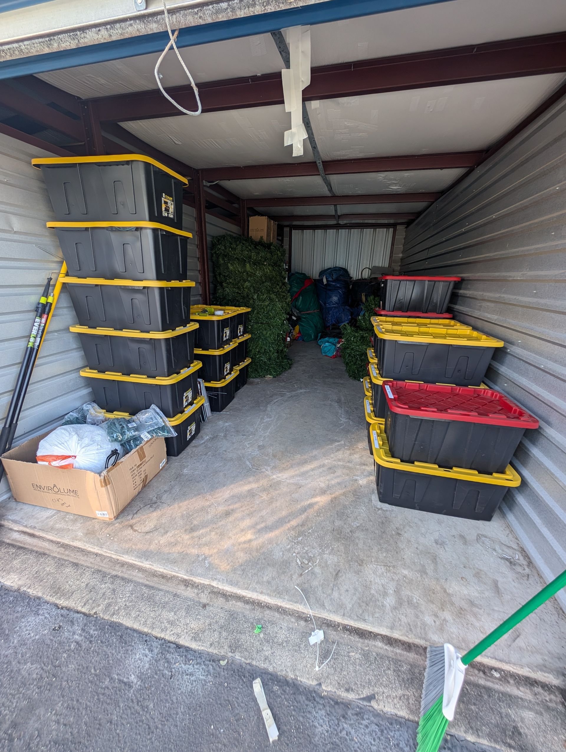 Storage unit filled with black and yellow/red bins, a Christmas tree, and boxes.
