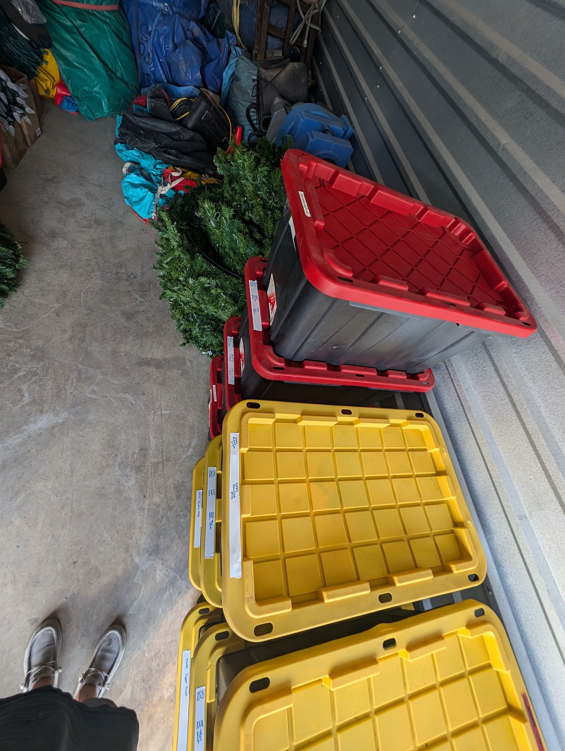 Storage unit with yellow and red bins stacked, artificial greenery, and various stored items.