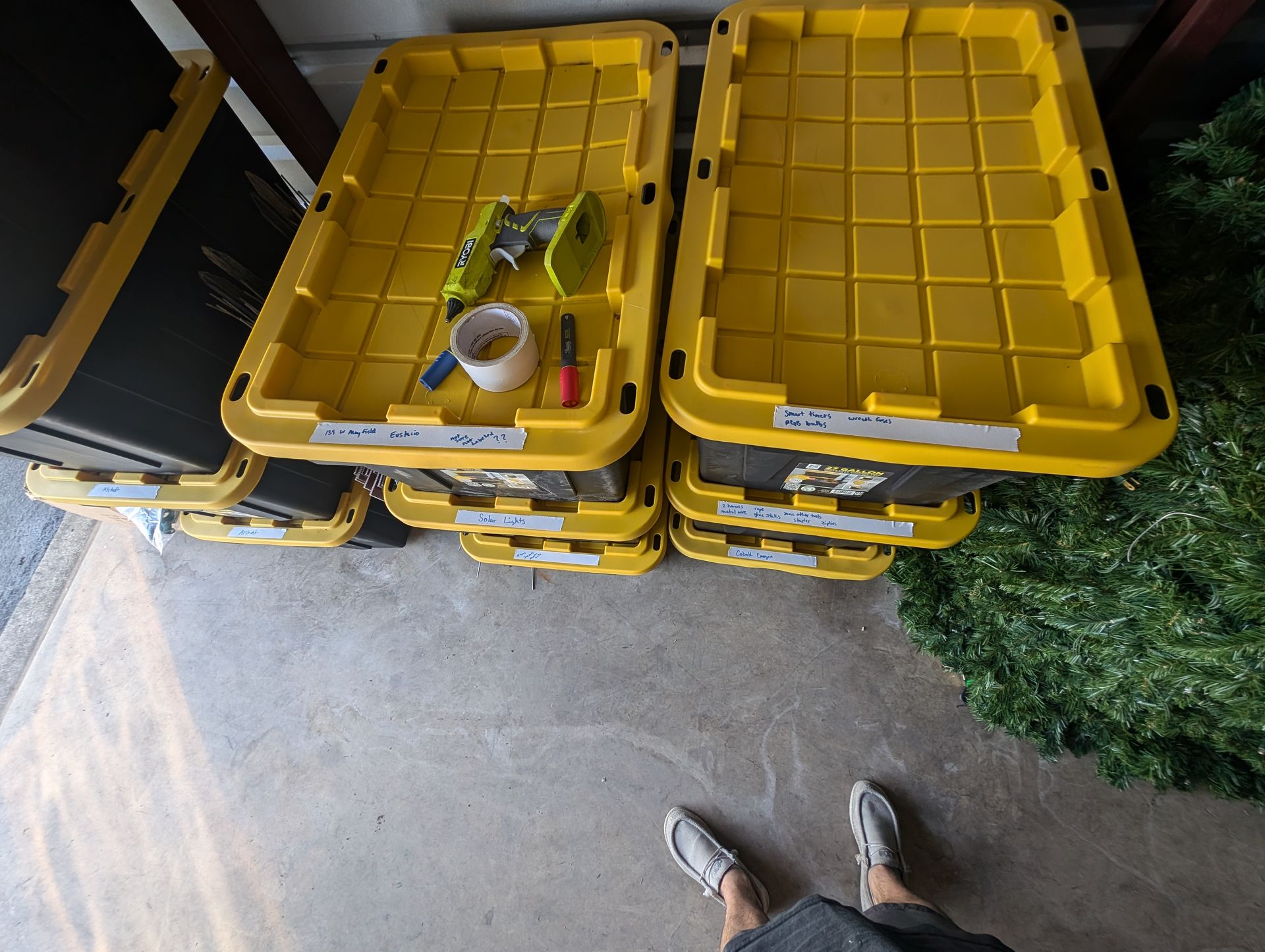 Yellow storage bins stacked; tools on one. Feet standing nearby on concrete.