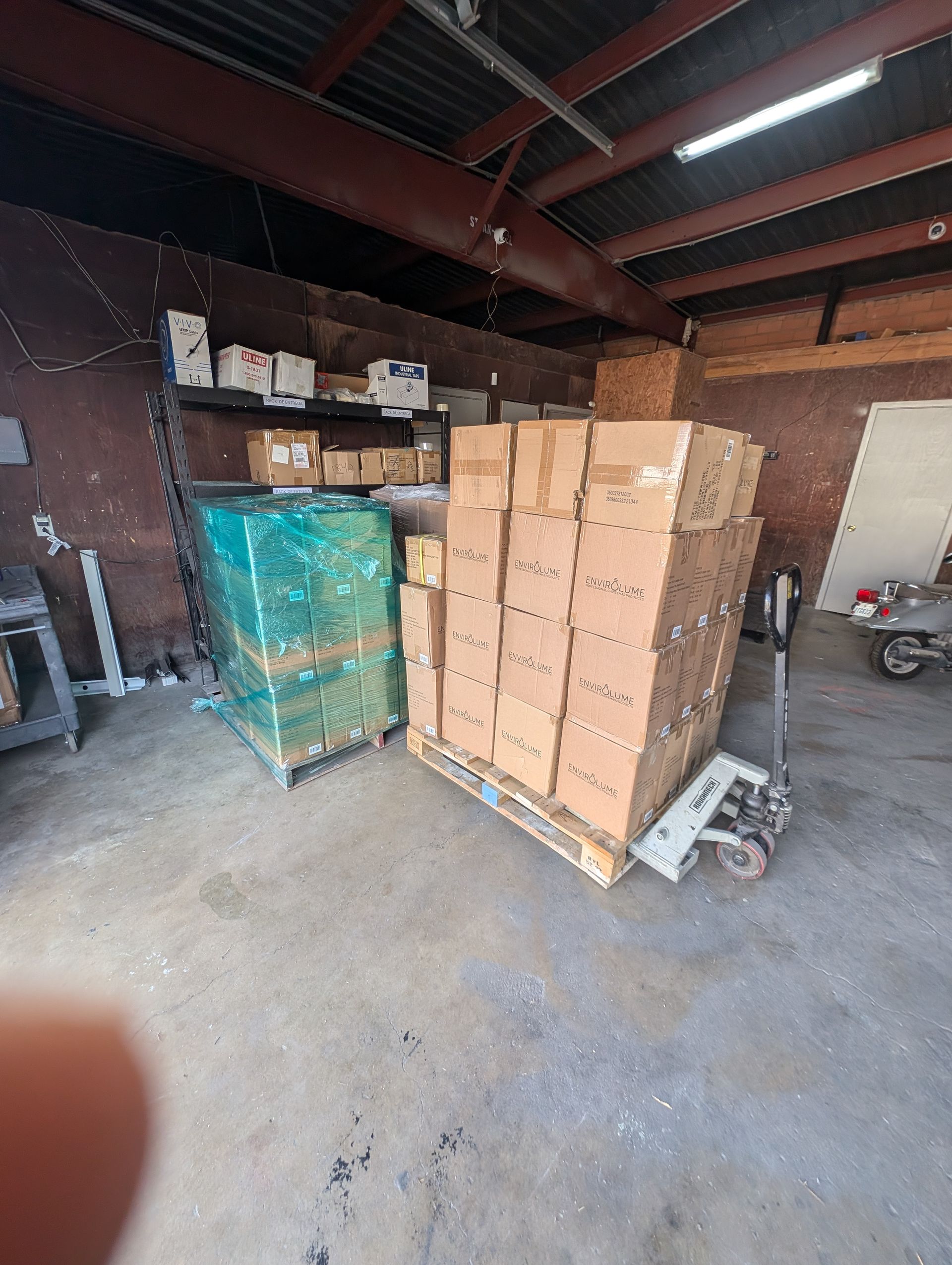 Boxes on a pallet in a warehouse, a green-wrapped pallet is next to it.