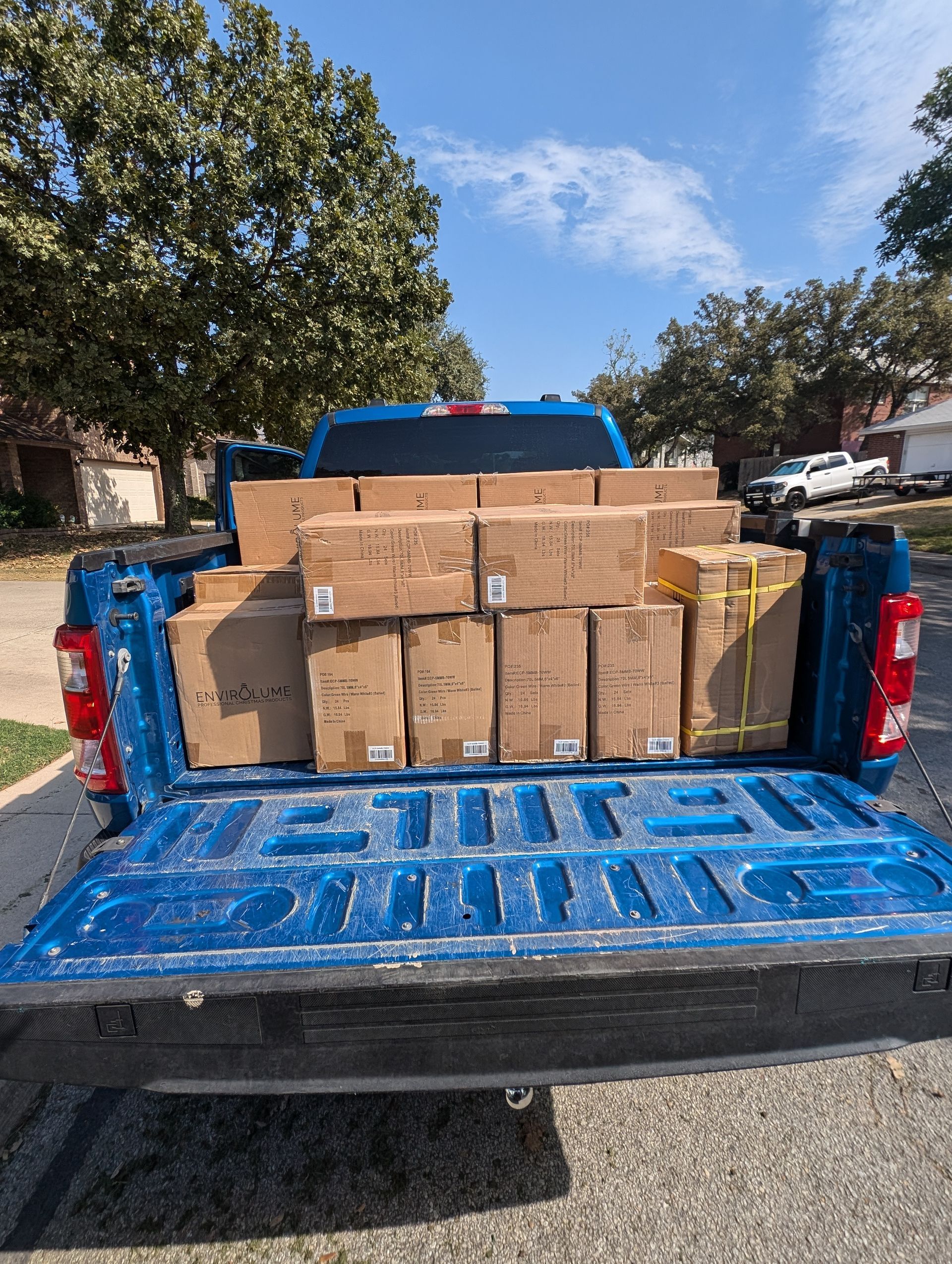 Blue truck bed filled with stacked cardboard boxes on a sunny day in a residential area.