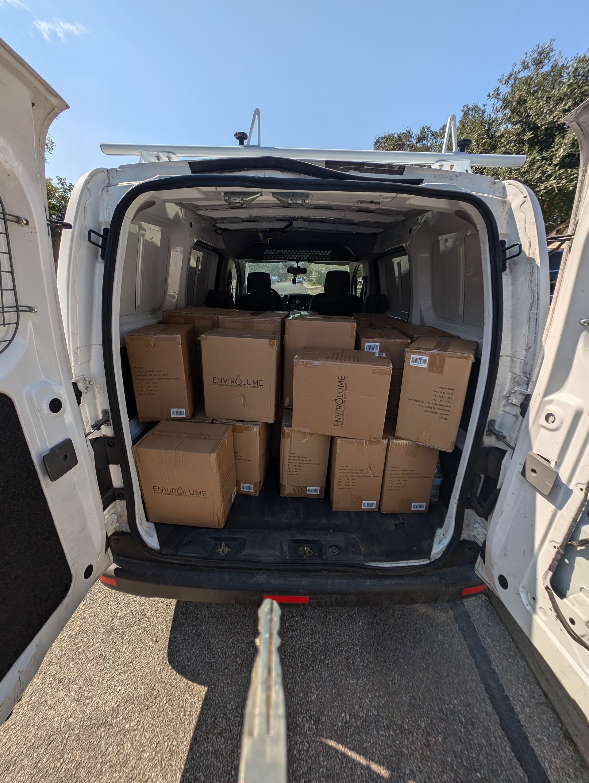 Van interior filled with cardboard boxes, rear doors open, on a sunny day.
