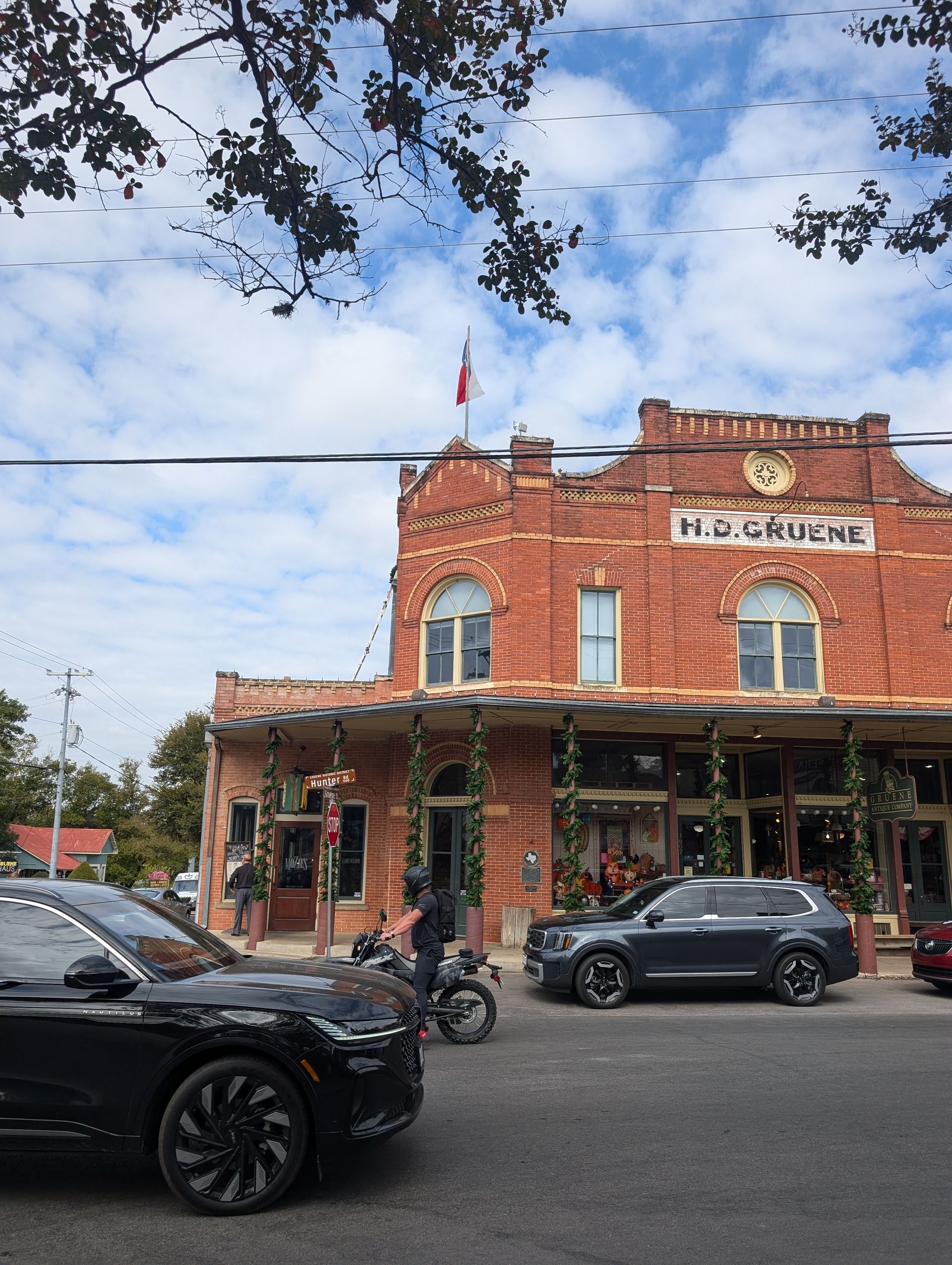 Red brick building with a Texas flag, cars parked in front.