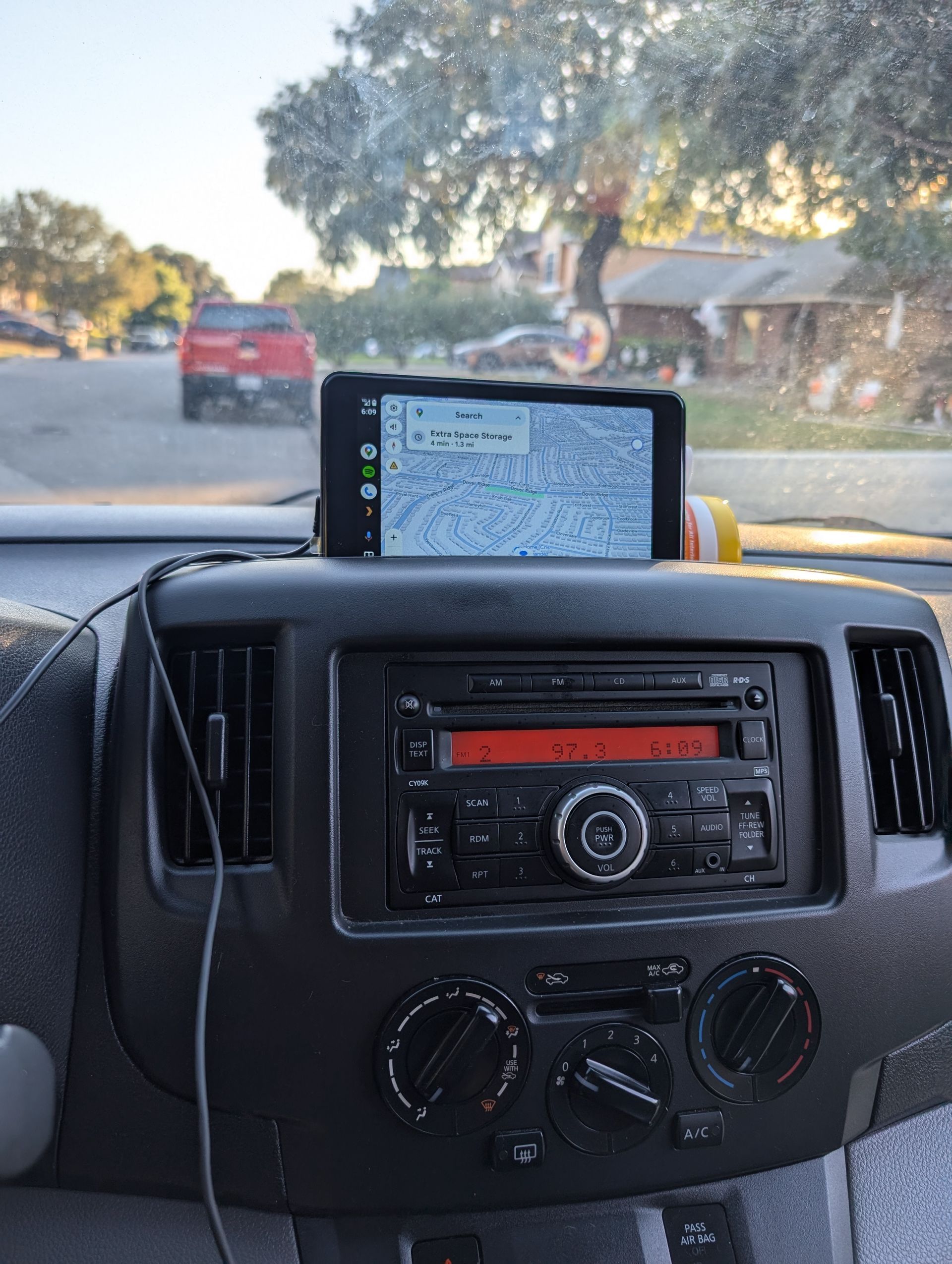 Dashboard of a vehicle with a phone displaying a map on top. The radio is visible. A street is seen outside.