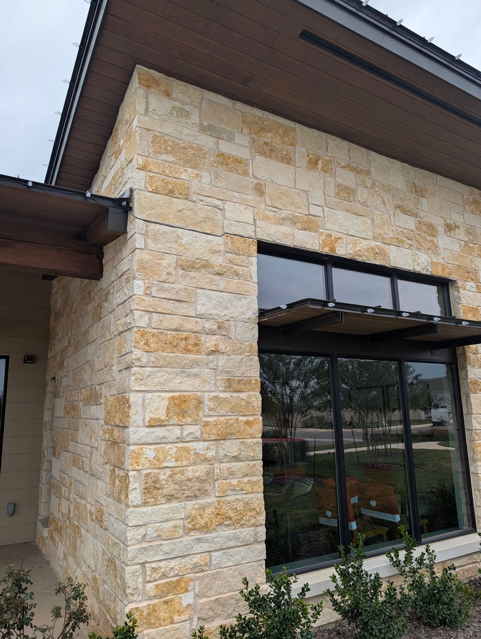 Beige stone building corner with dark-framed windows, under a brown roof.