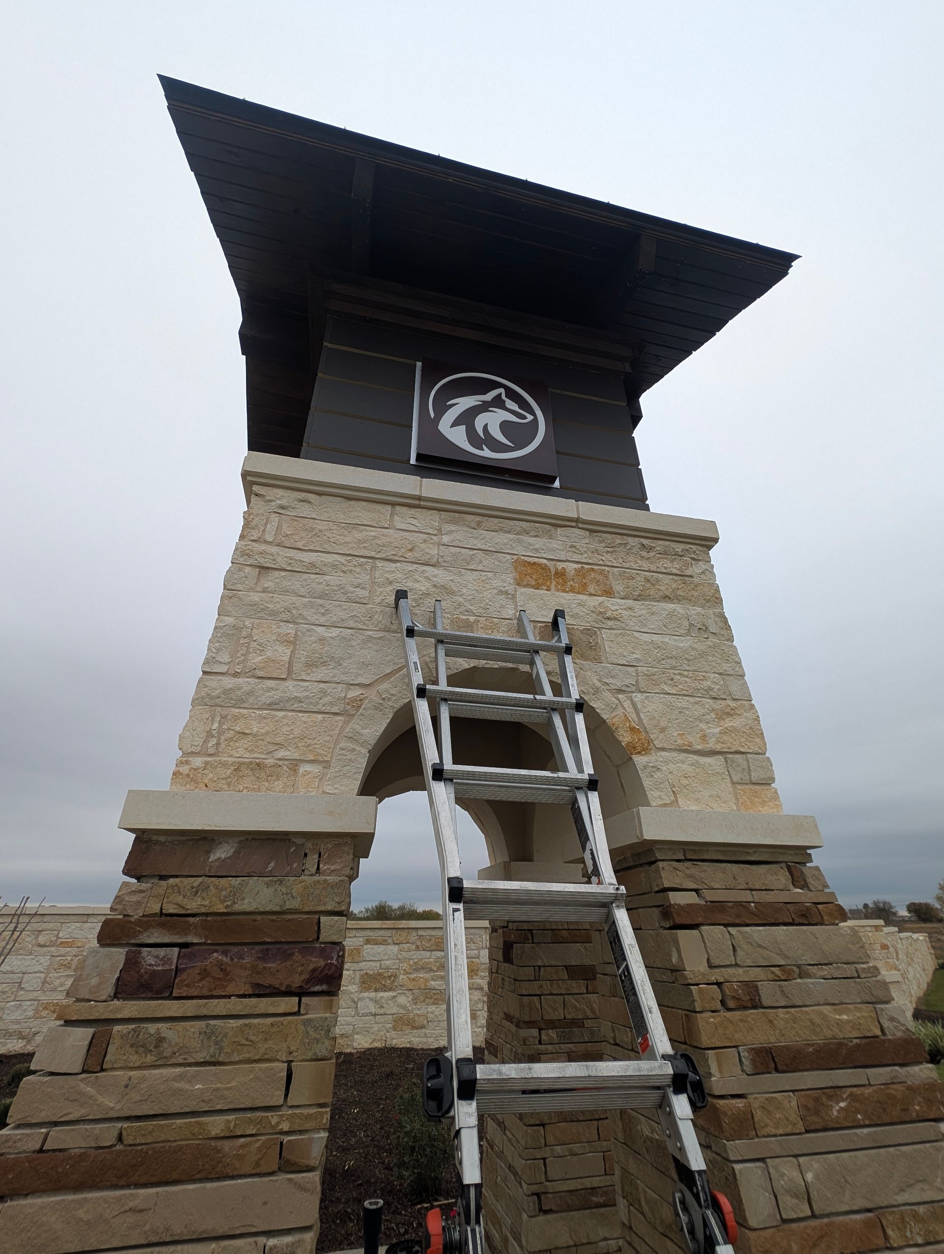 Stone archway with ladder leaning against it; sign with cougar logo on top.