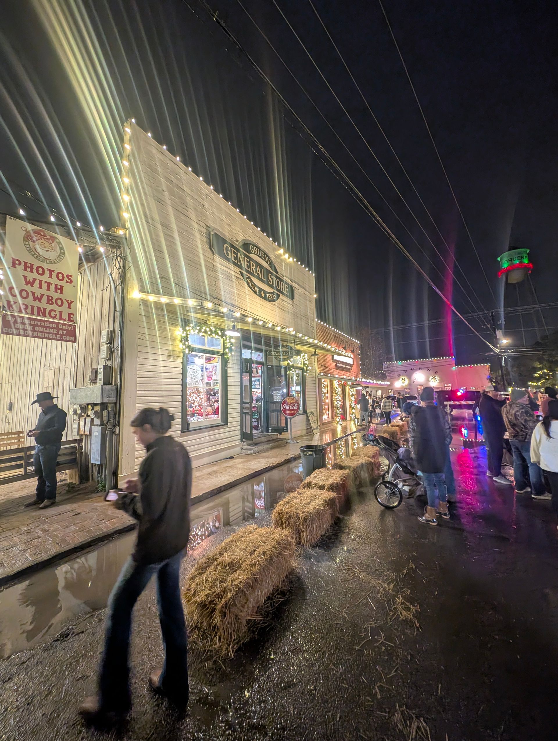 Nighttime scene with Hard Rock Cafe and people; building decorated with lights, wet street.