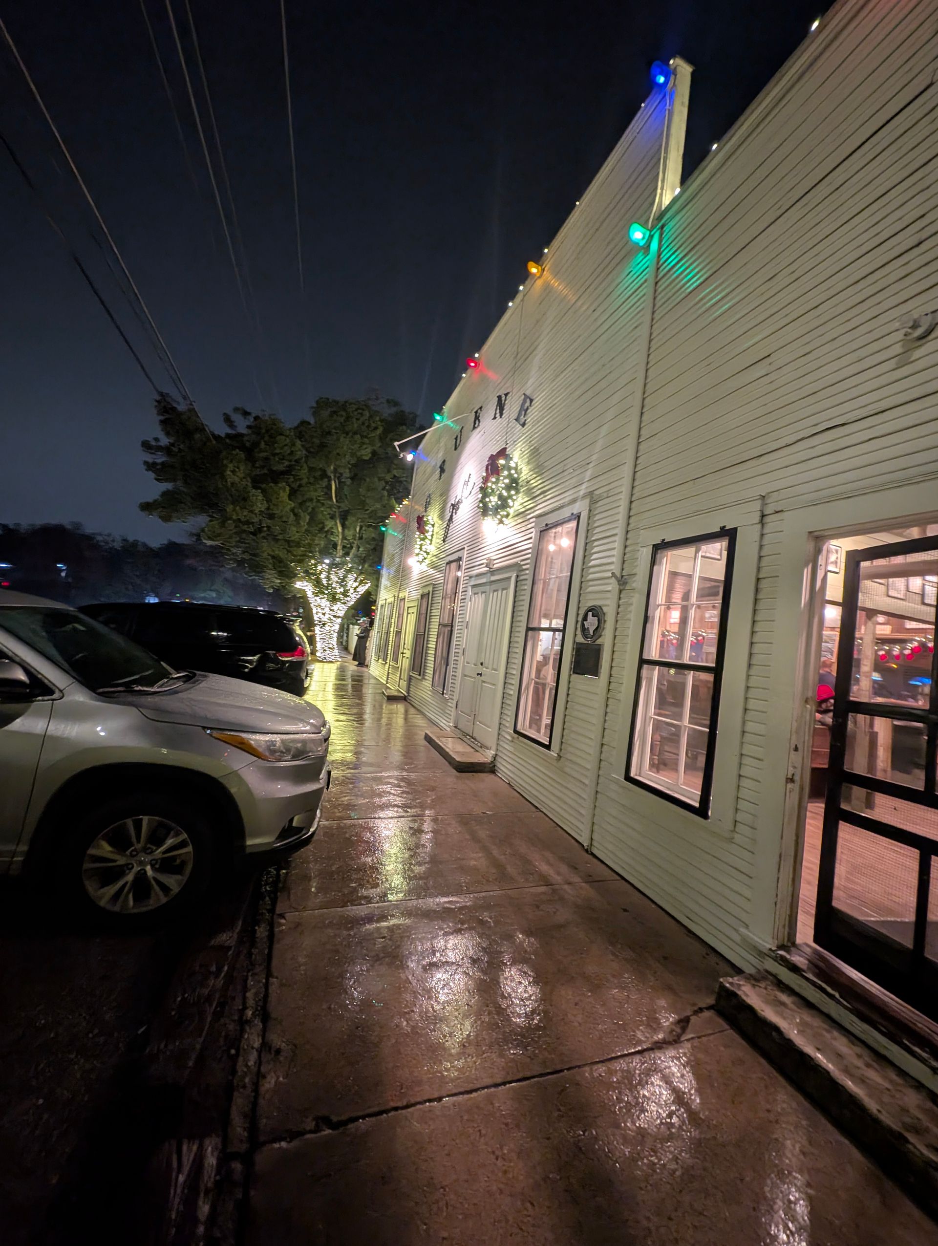 A white building with lit windows at night. Cars are parked in front of the building.